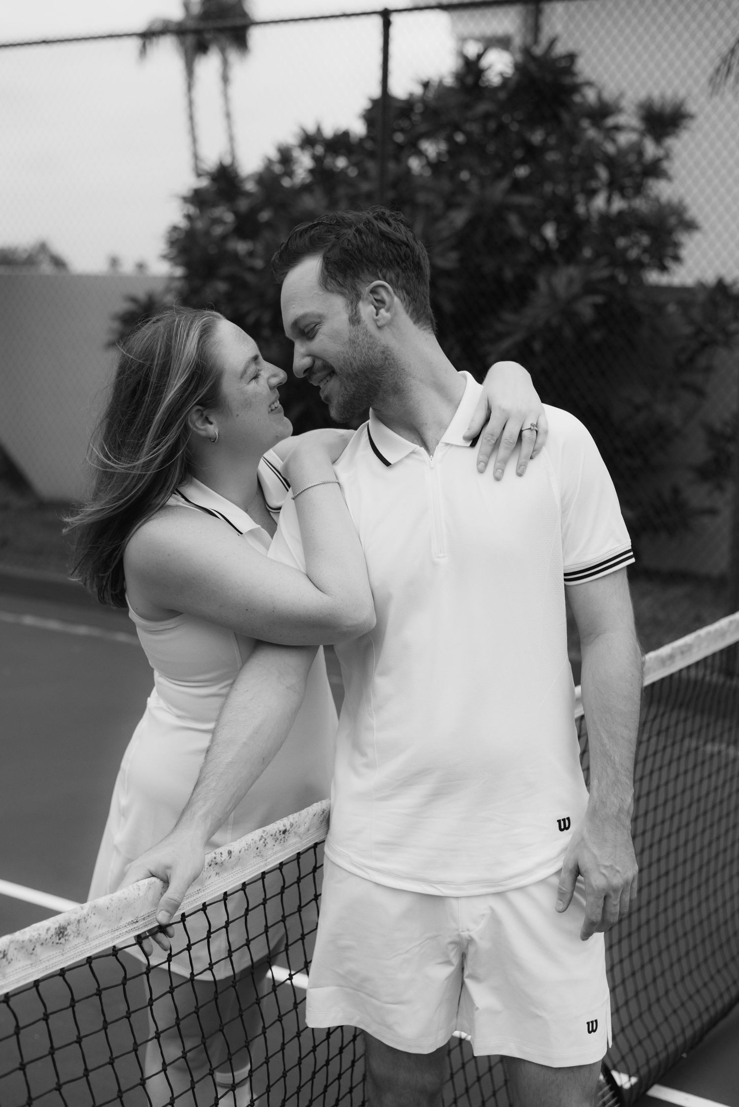 Romantic couple embracing by tennis net during outdoor match.