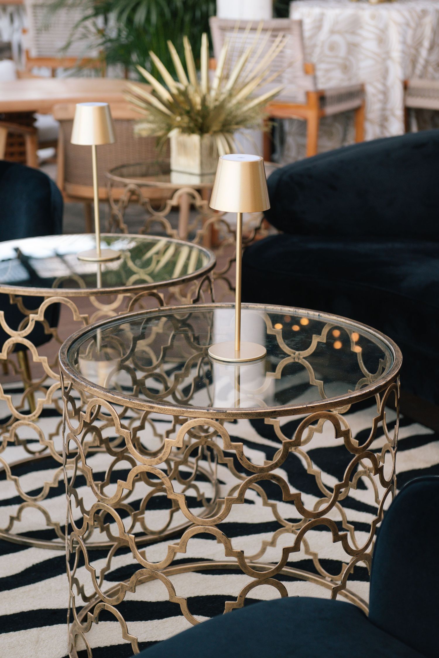 Elegant glass and gold side table with intricate metalwork pattern and small table lamps in a modern living space.