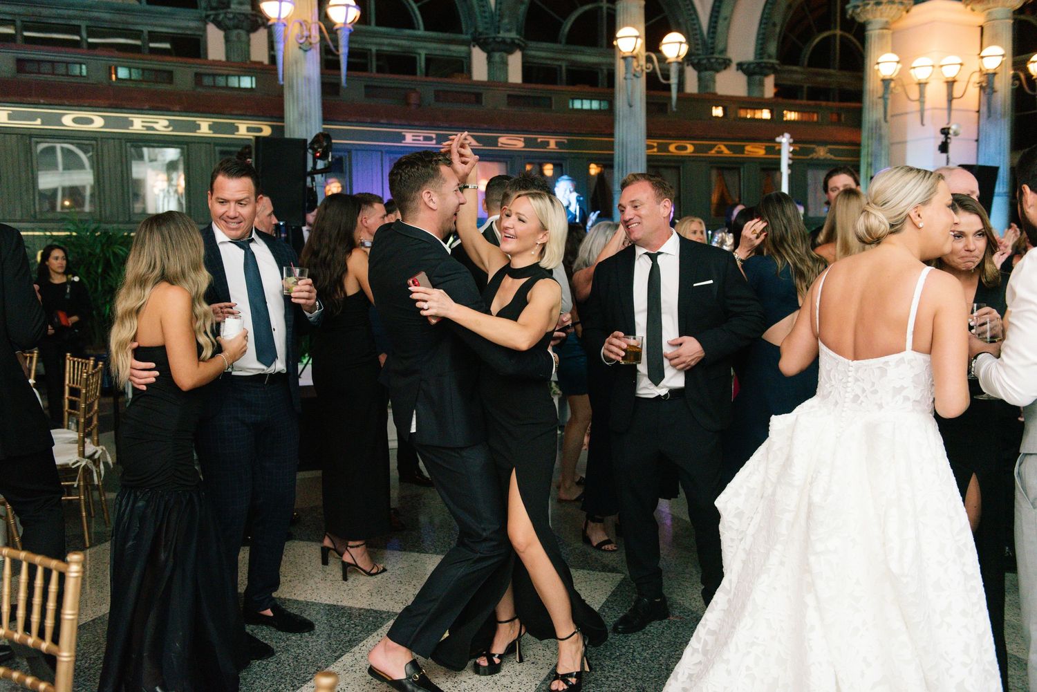 Guests dancing at lively wedding reception in grand historic venue.