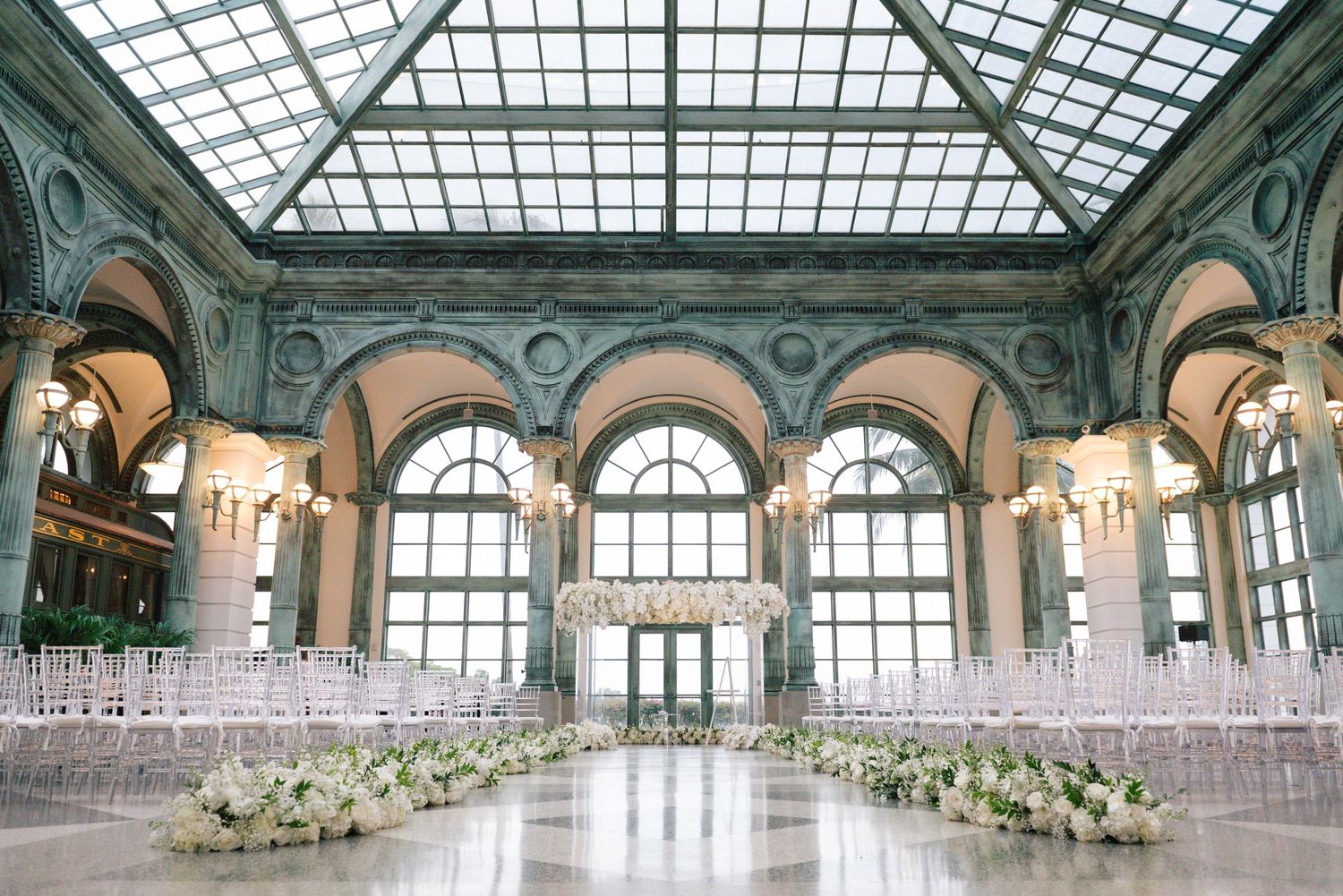 Grand ballroom with glass ceiling and ornate architecture set up for an elegant wedding ceremony.