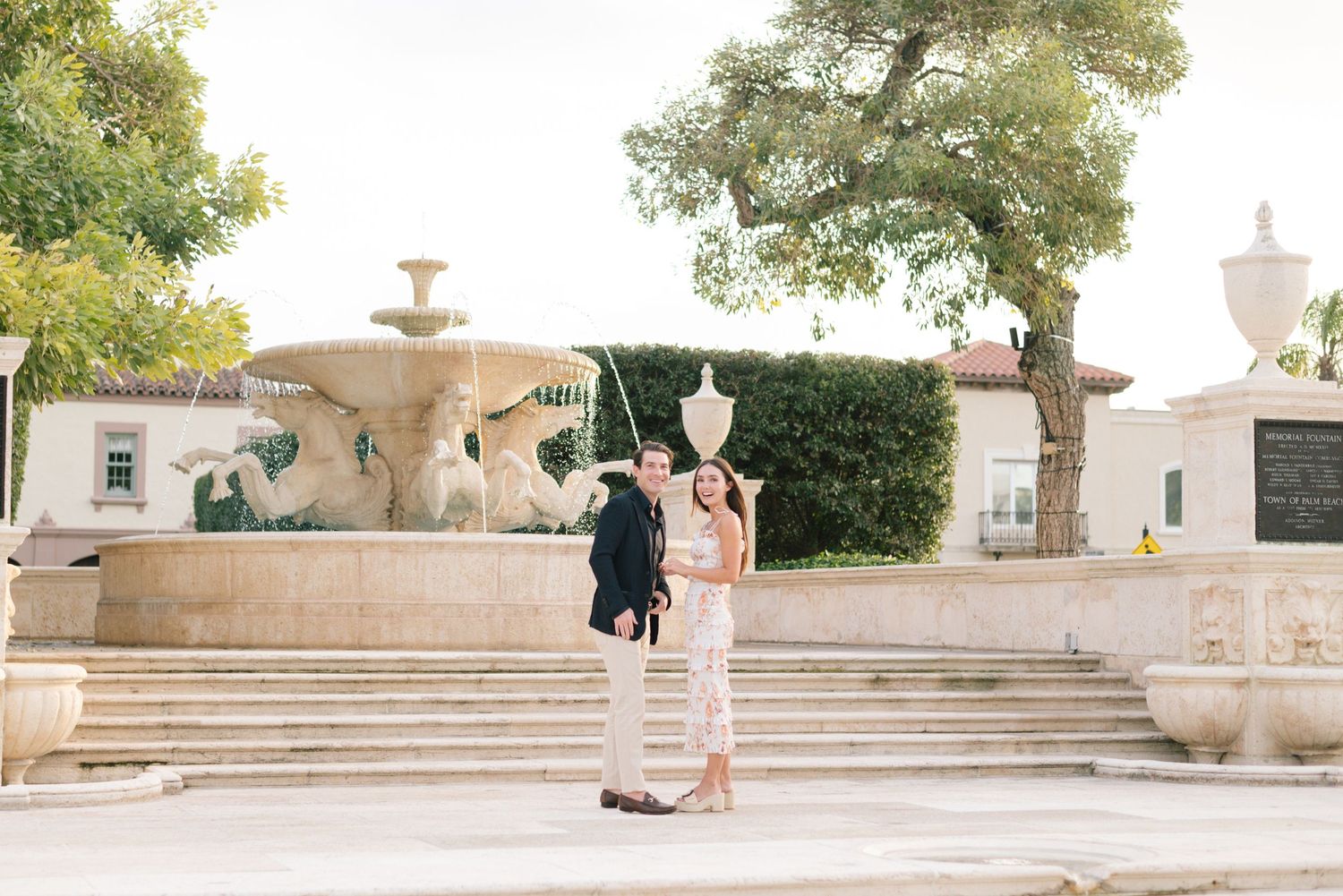 A panoramic view of a stone fountain and courtyard with ornate architectural details and landscaping in the background.
