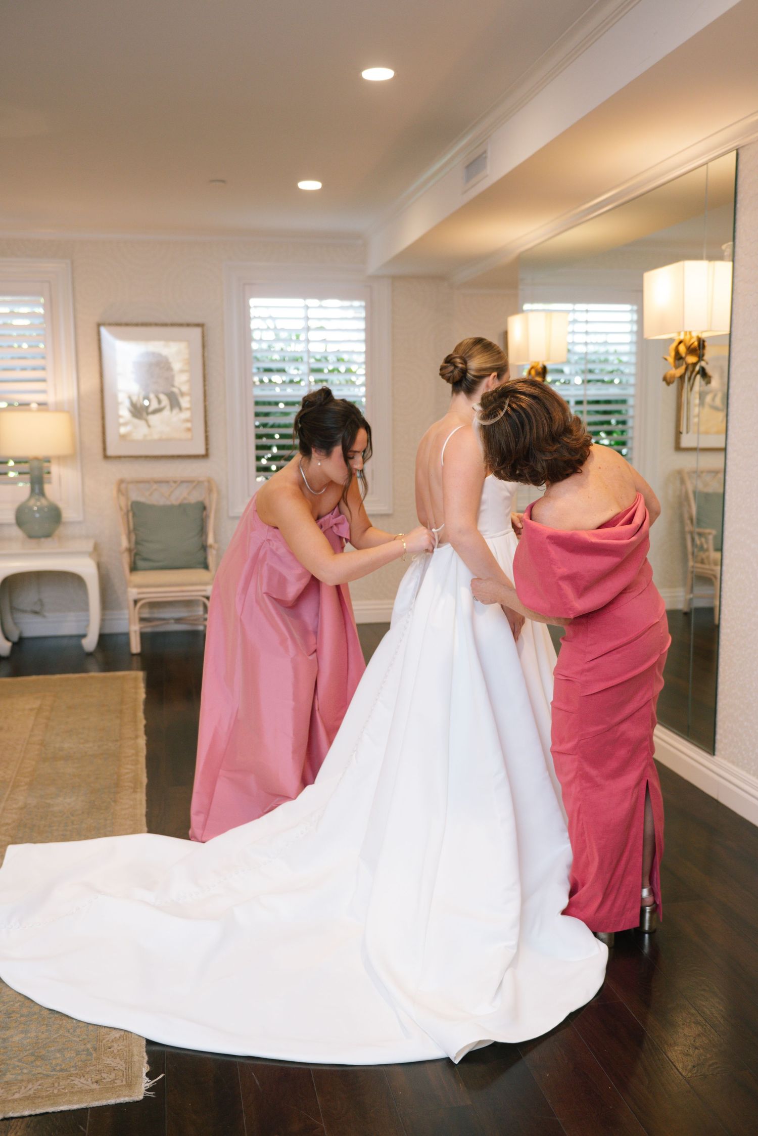Bridesmaids help adjust a white wedding dress train in an elegant indoor setting.