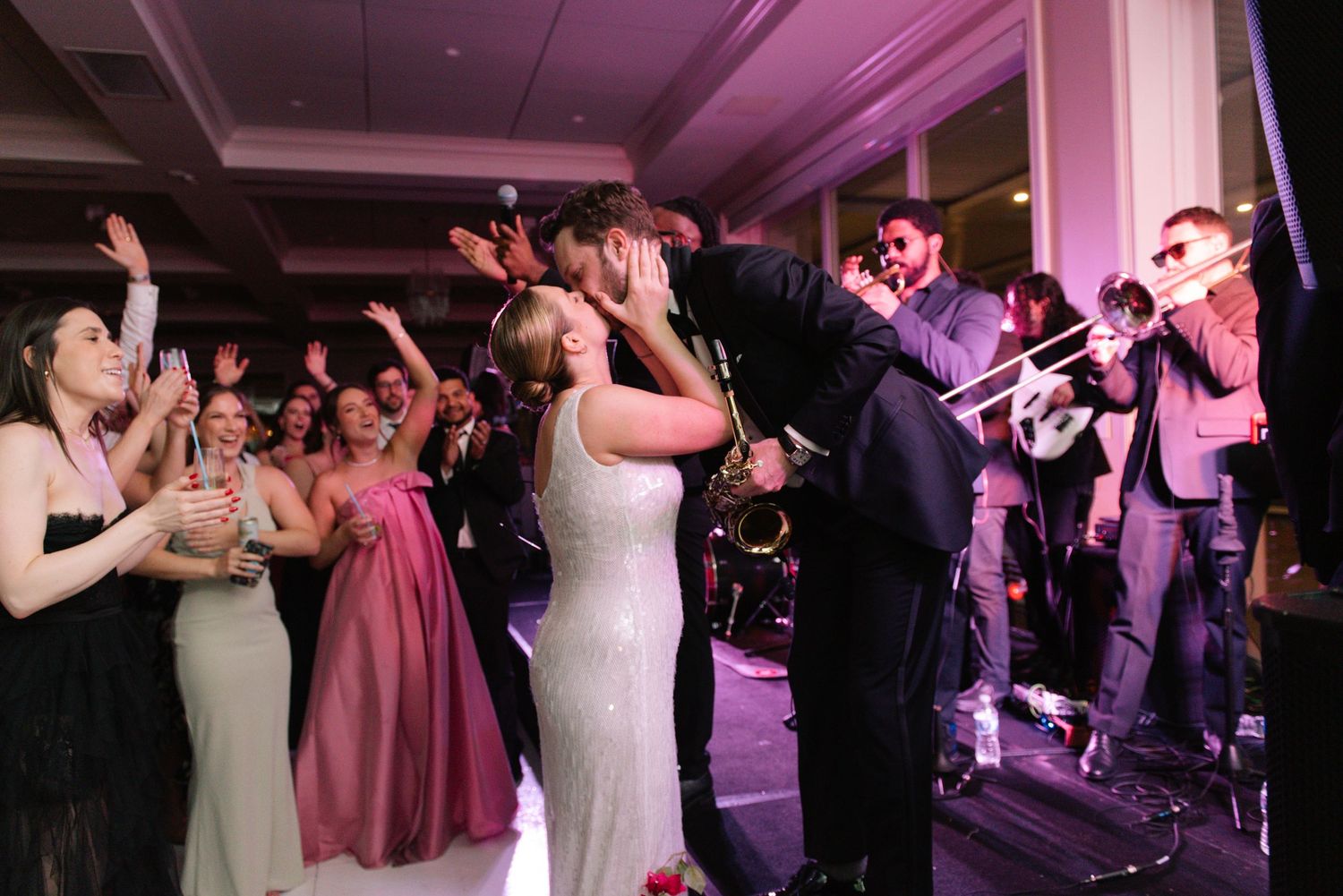 Energetic dance floor scene at a wedding reception with purple ambient lighting.