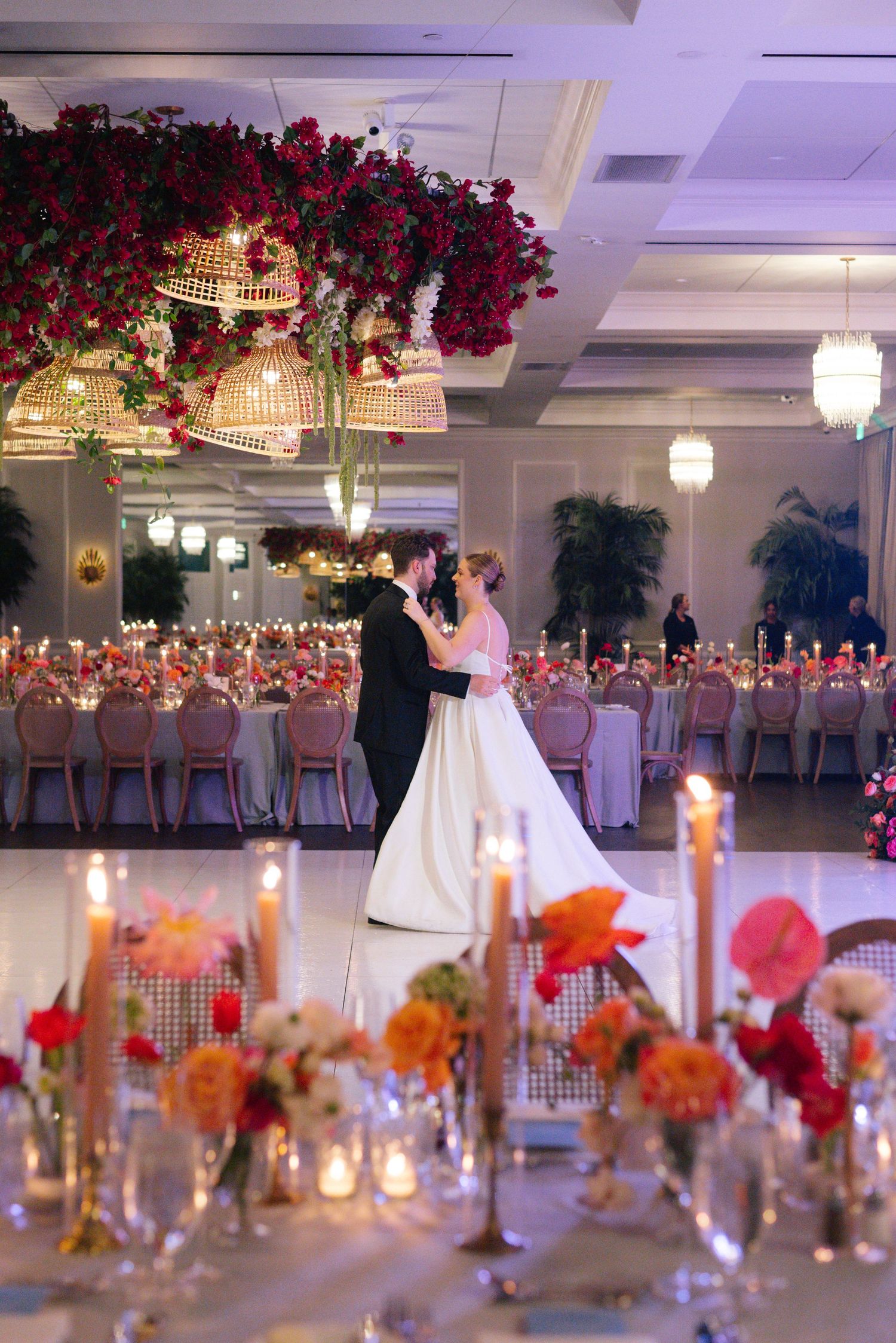 Elegant ballroom wedding reception with dramatic red floral arrangements and crystal chandeliers.