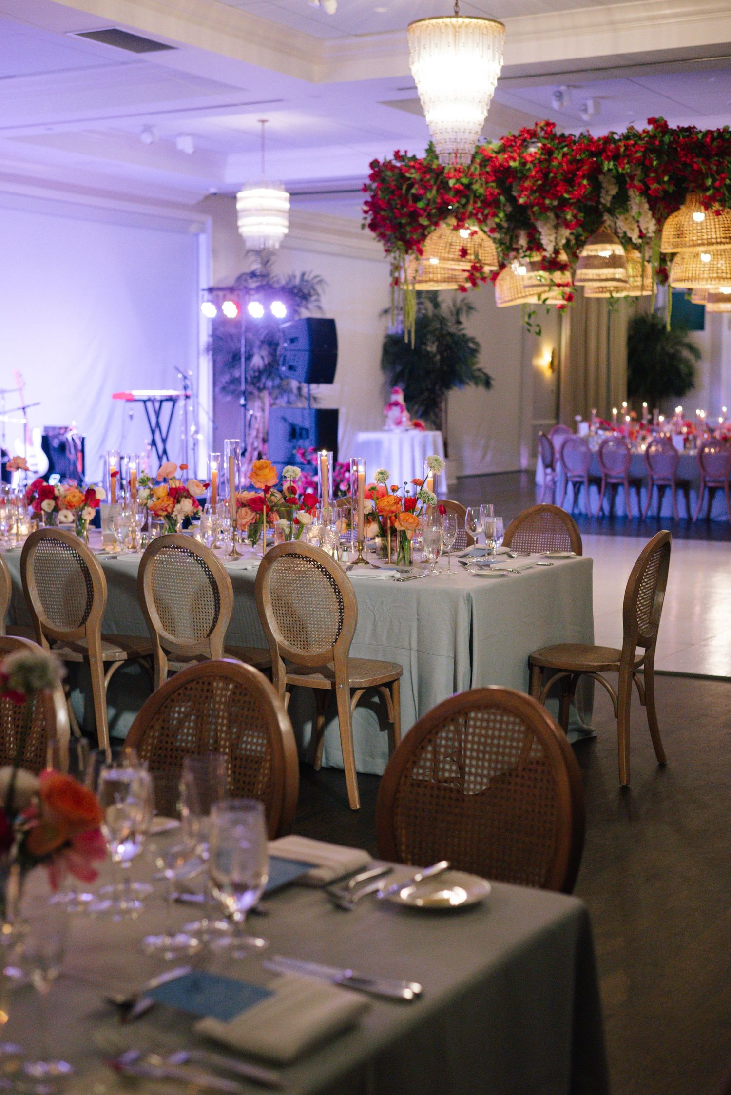 Elegant wedding reception ballroom with crystal chandeliers, round tables, and red floral centerpieces.
