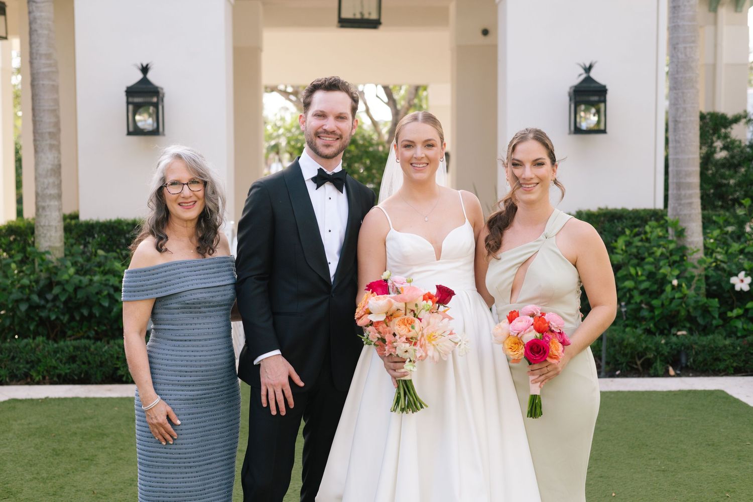 Wedding group portrait in front of white colonial building with black lanterns.
