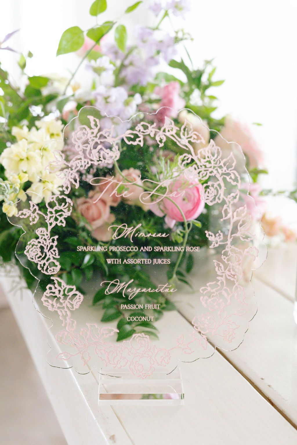 Decorative acrylic menu card with floral design displayed among pink and white flower arrangements.