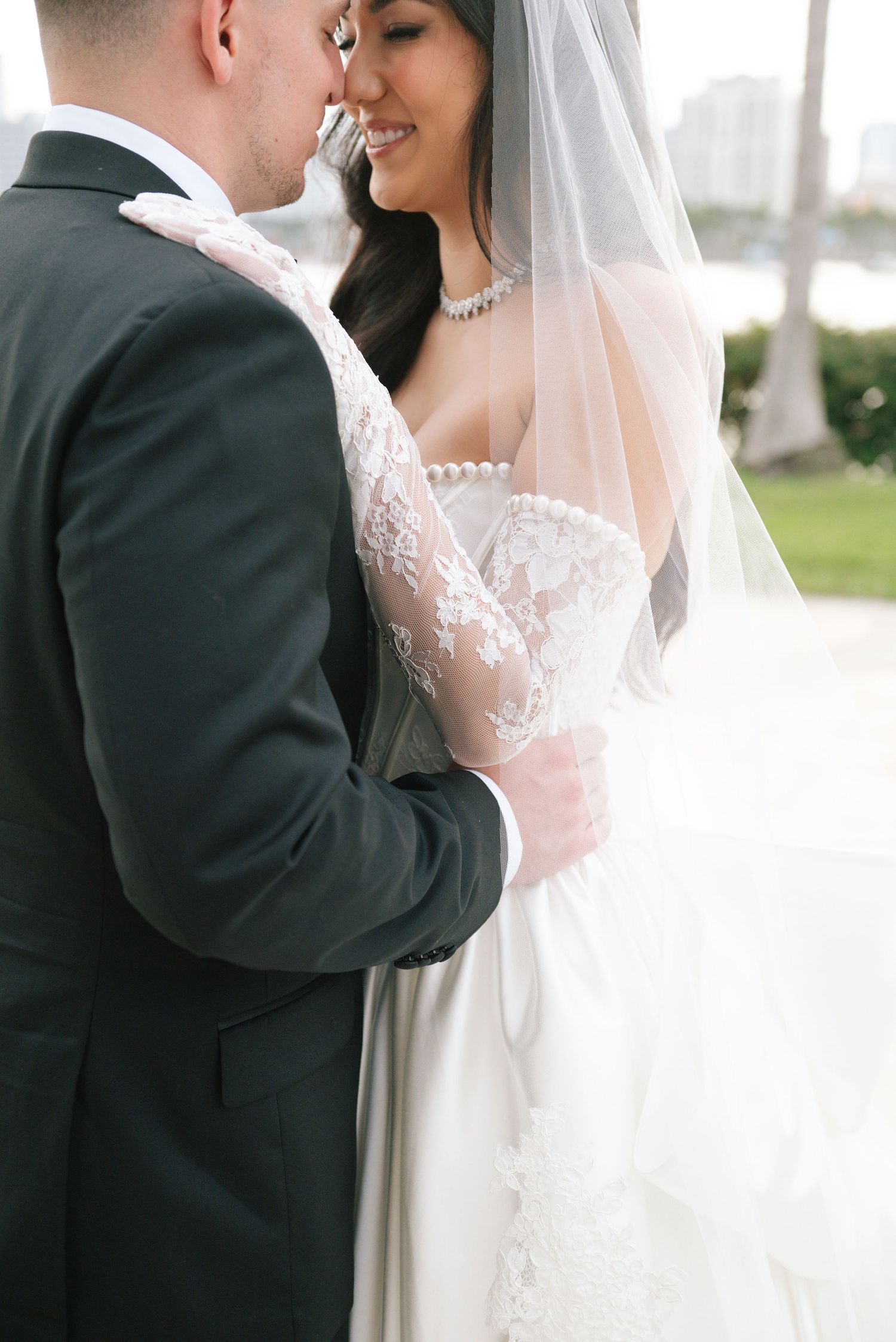 An intimate wedding moment captured with a flowing white veil against a bright outdoor background.