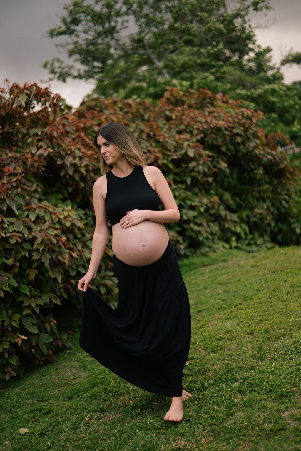 Artistic maternity photos captured in a lush garden setting with flowing black dress.