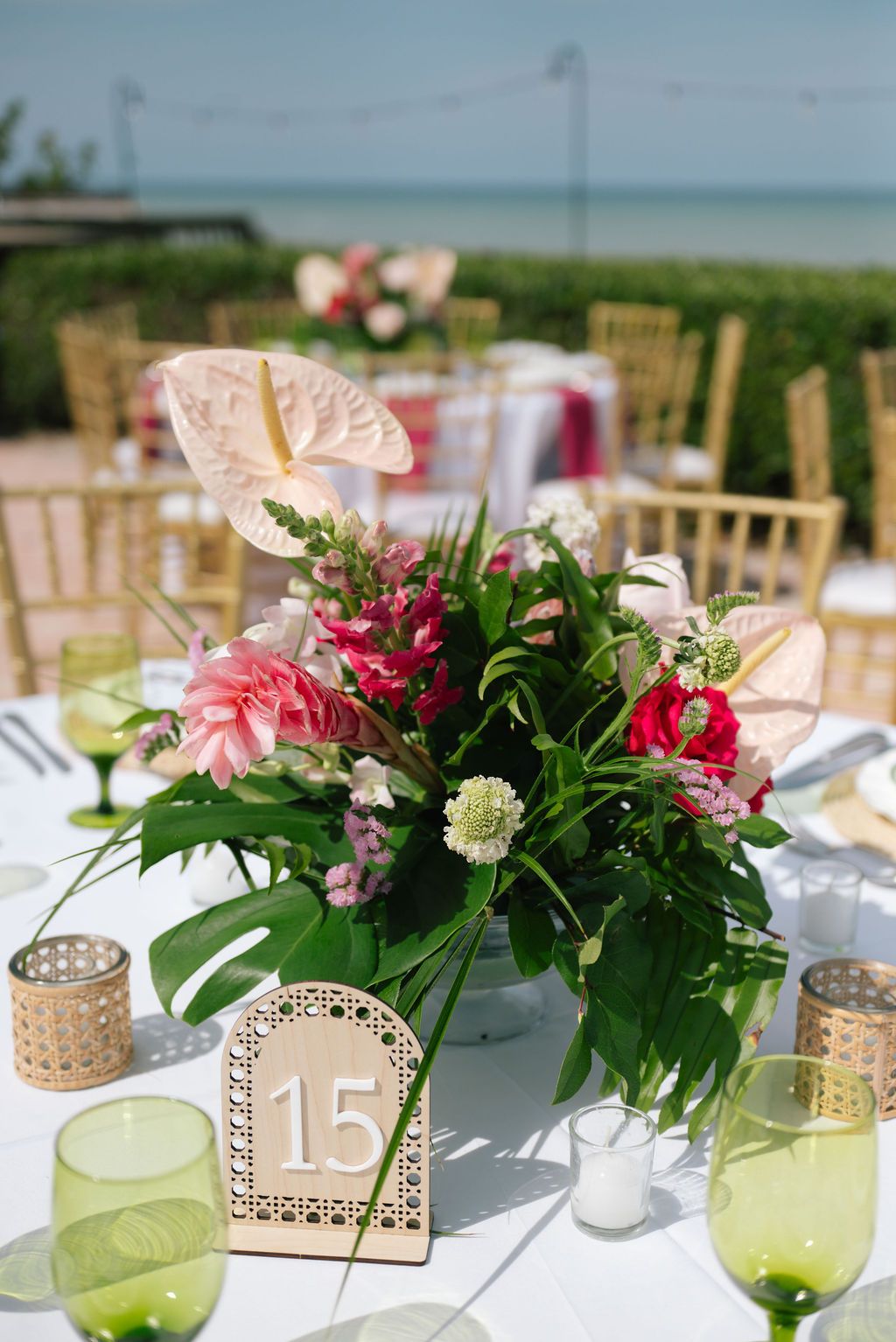 Wedding table settings with floral centerpieces, table numbers, and green glassware.