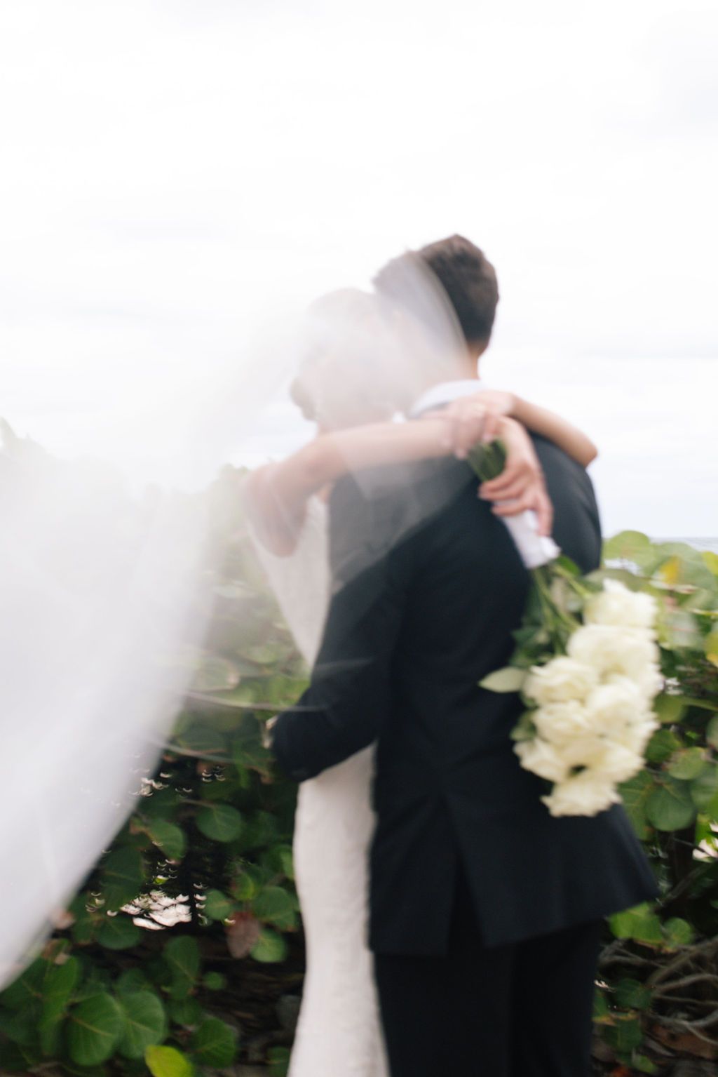 Bride and groom share a tender moment among white flowers and greenery.