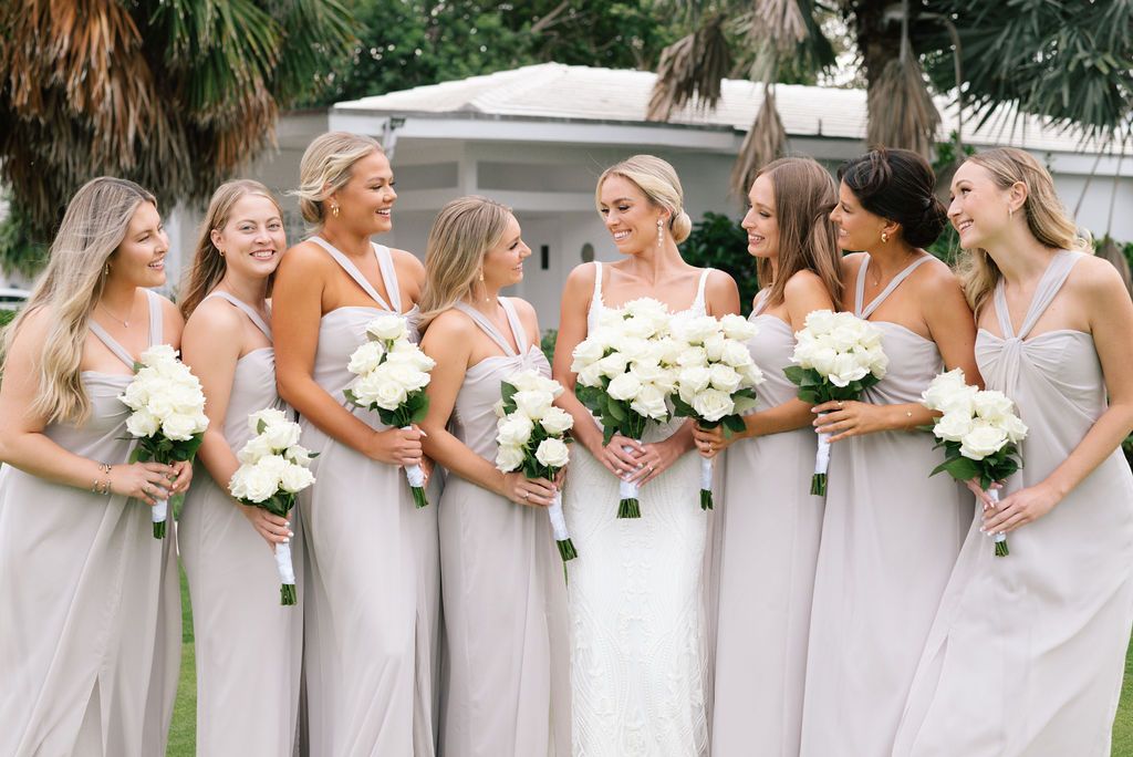 Bridesmaids in light gray dresses hold white bouquets in outdoor wedding setting.