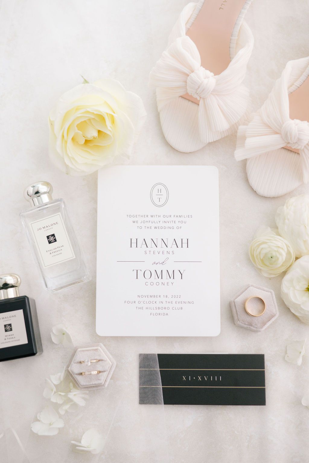 Elegant wedding invitation suite with perfume bottles and white roses on light marble background.