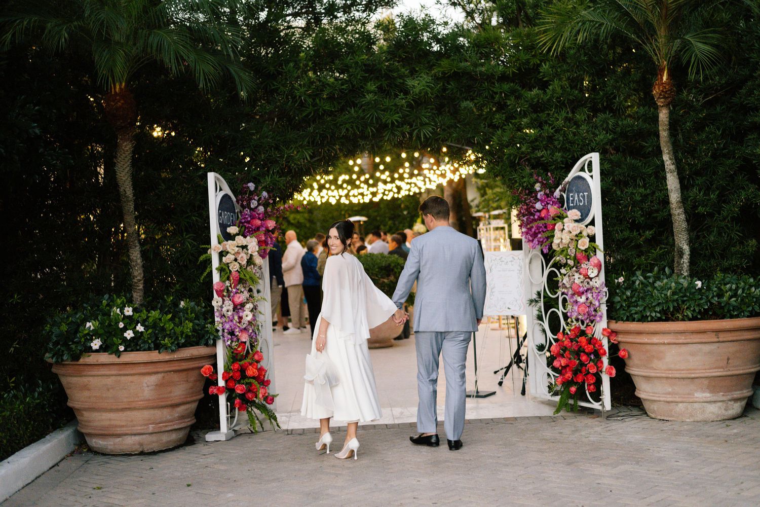 Garden wedding venue with string lights and large potted plants along pathway.