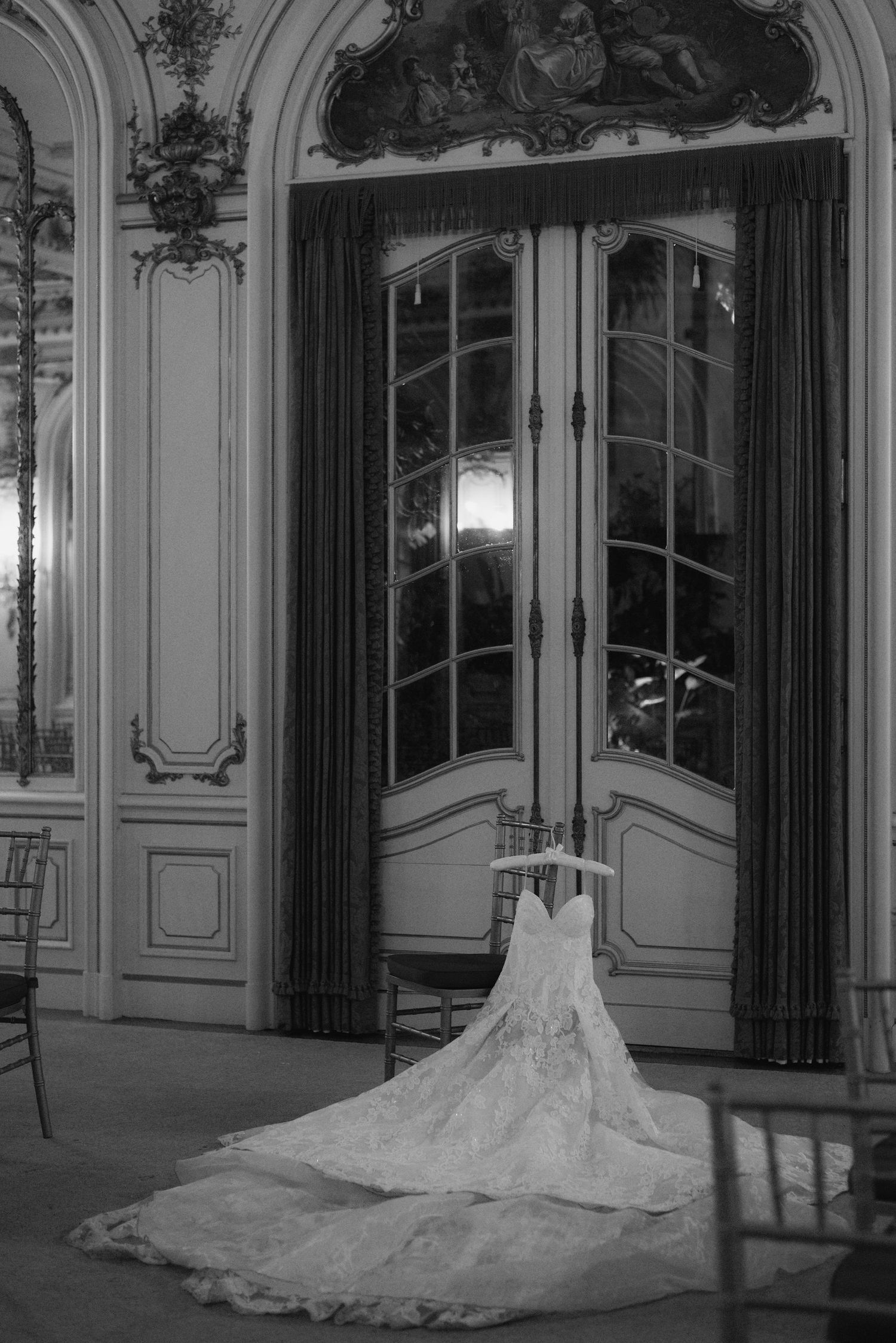 Elegant white wedding dress with long train displayed in ornate ballroom with decorative moldings.