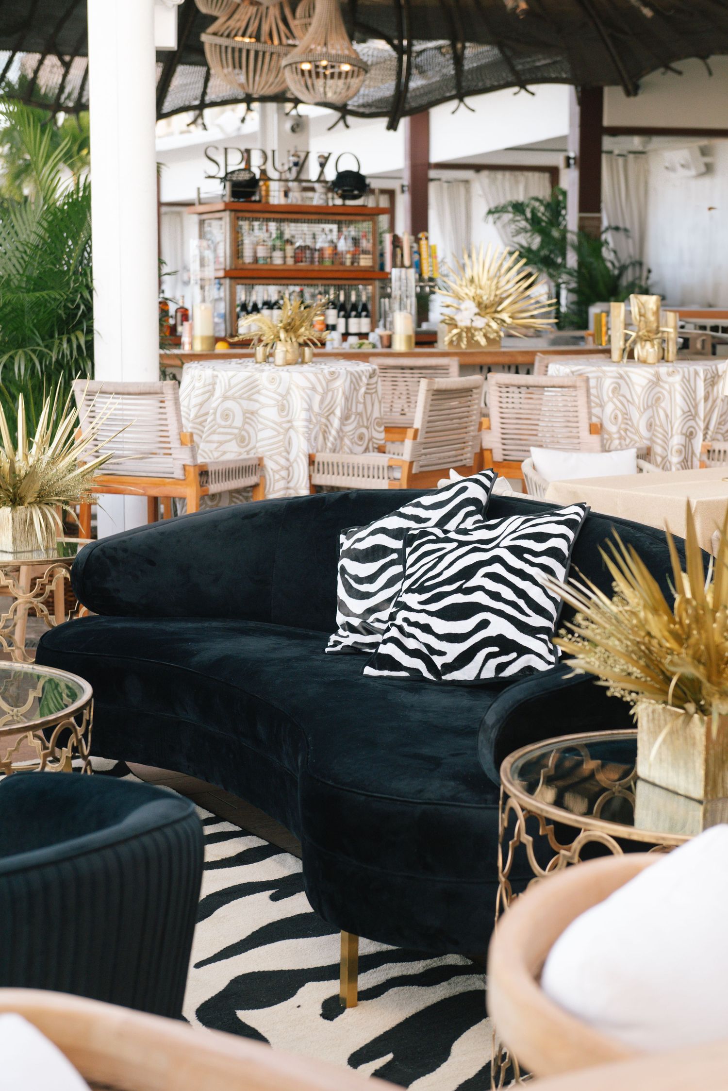 Modern event space featuring black velvet couches with zebra print pillows and golden decor accents.