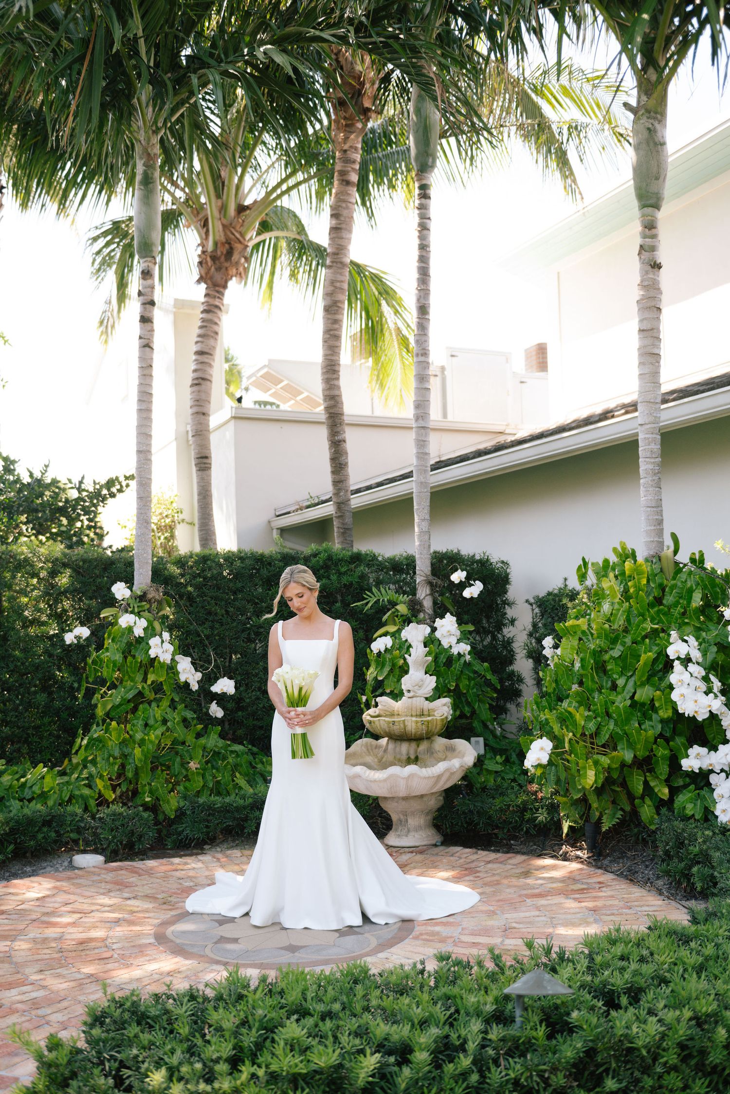 Wedding dress silhouette against tropical garden with fountain and palm trees.