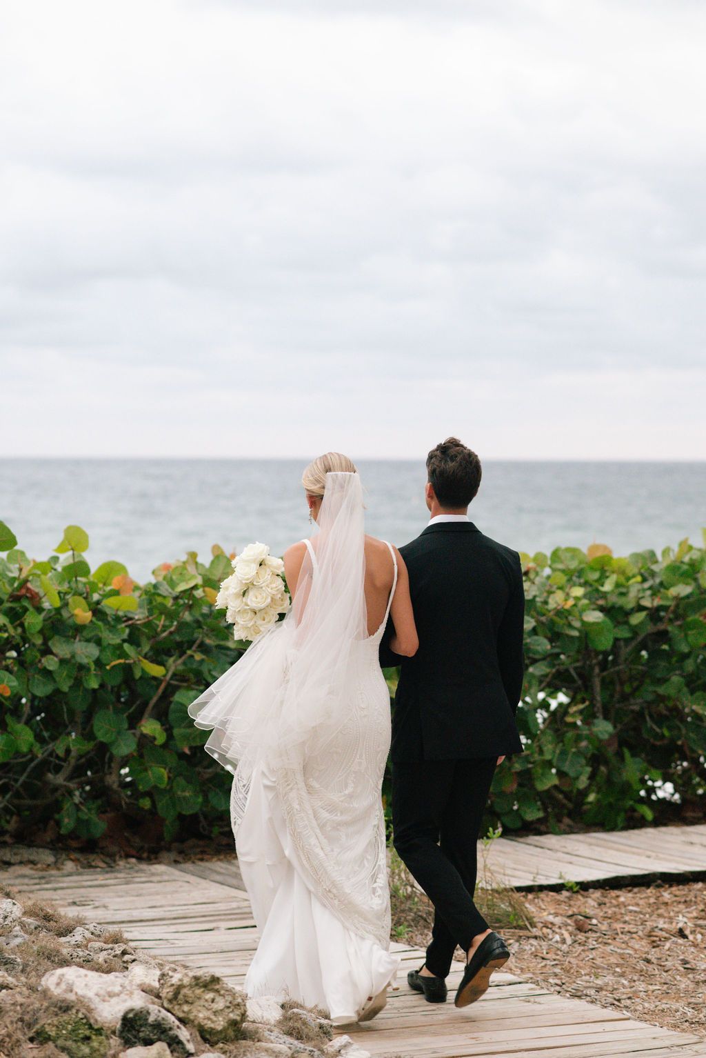 Couple walking along coastal boardwalk with ocean view.