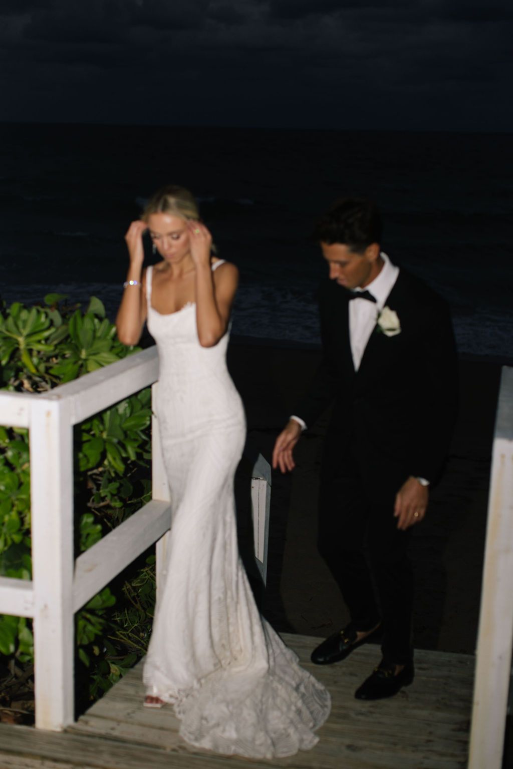 Couple in wedding attire photographed at dusk on beachfront deck.