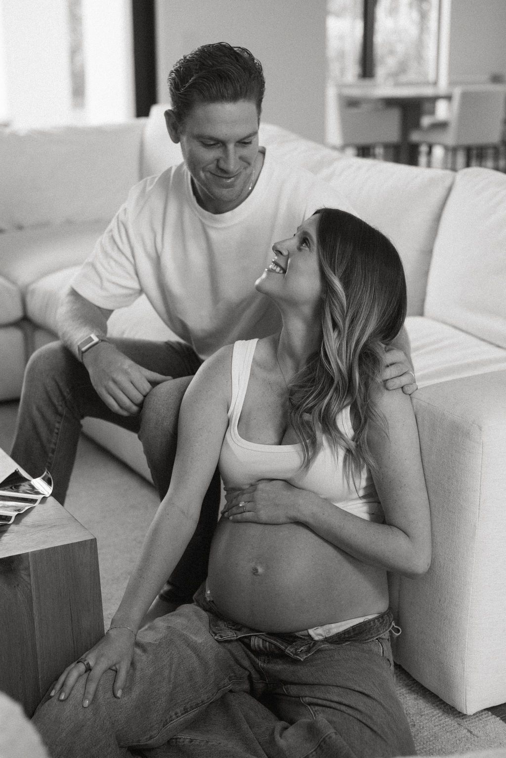 Black and white photo of expecting couple sharing tender moment on couch.