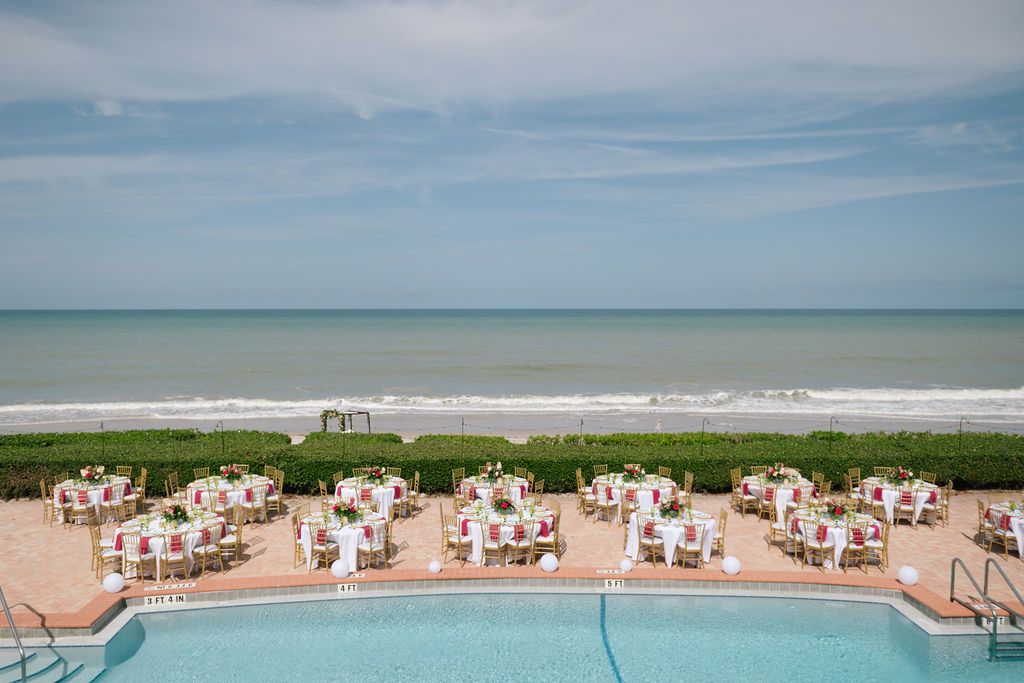 Panoramic view of a beachfront swimming pool with lounge chairs and ocean in the background.