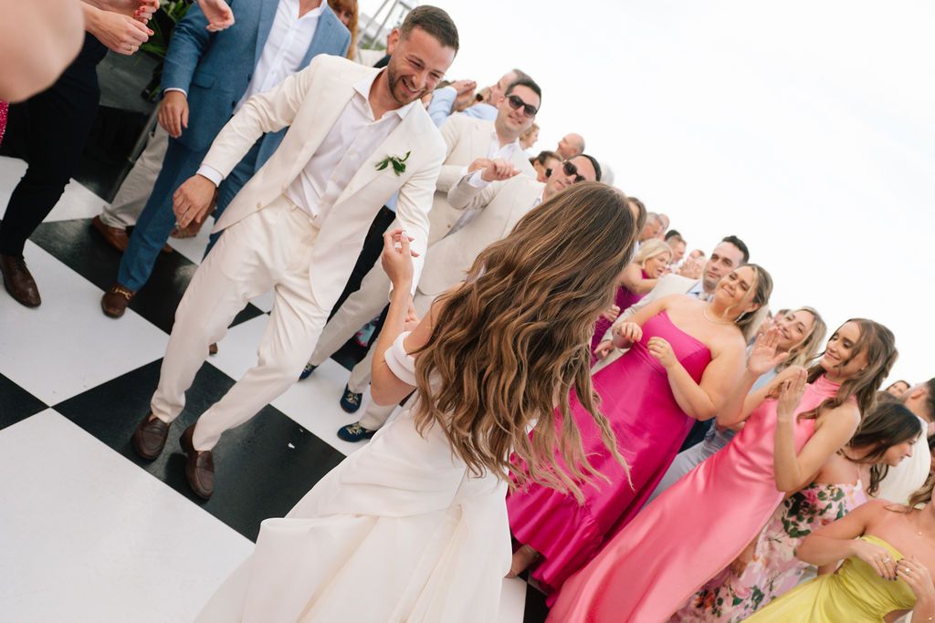 Energetic dance party with guests in formal attire on a black and white checkered floor.