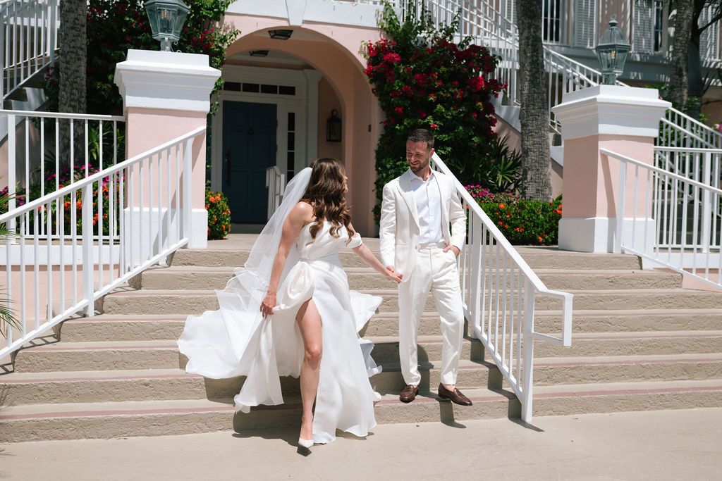 A bride's white dress flows gracefully down stone steps at an elegant venue entrance.