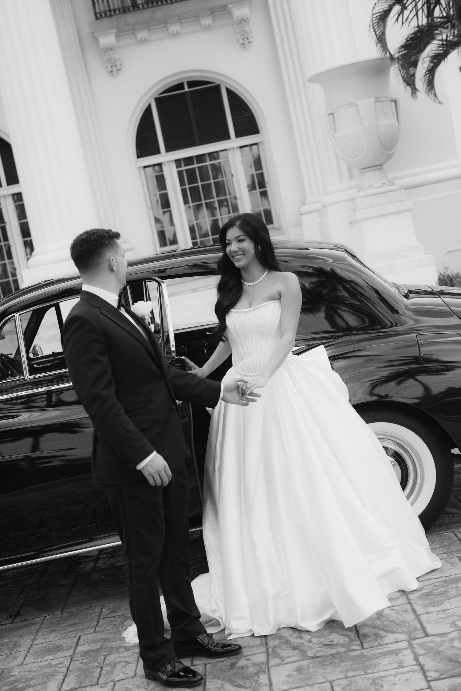 Black and white wedding photos with couple by vintage car at colonial venue.