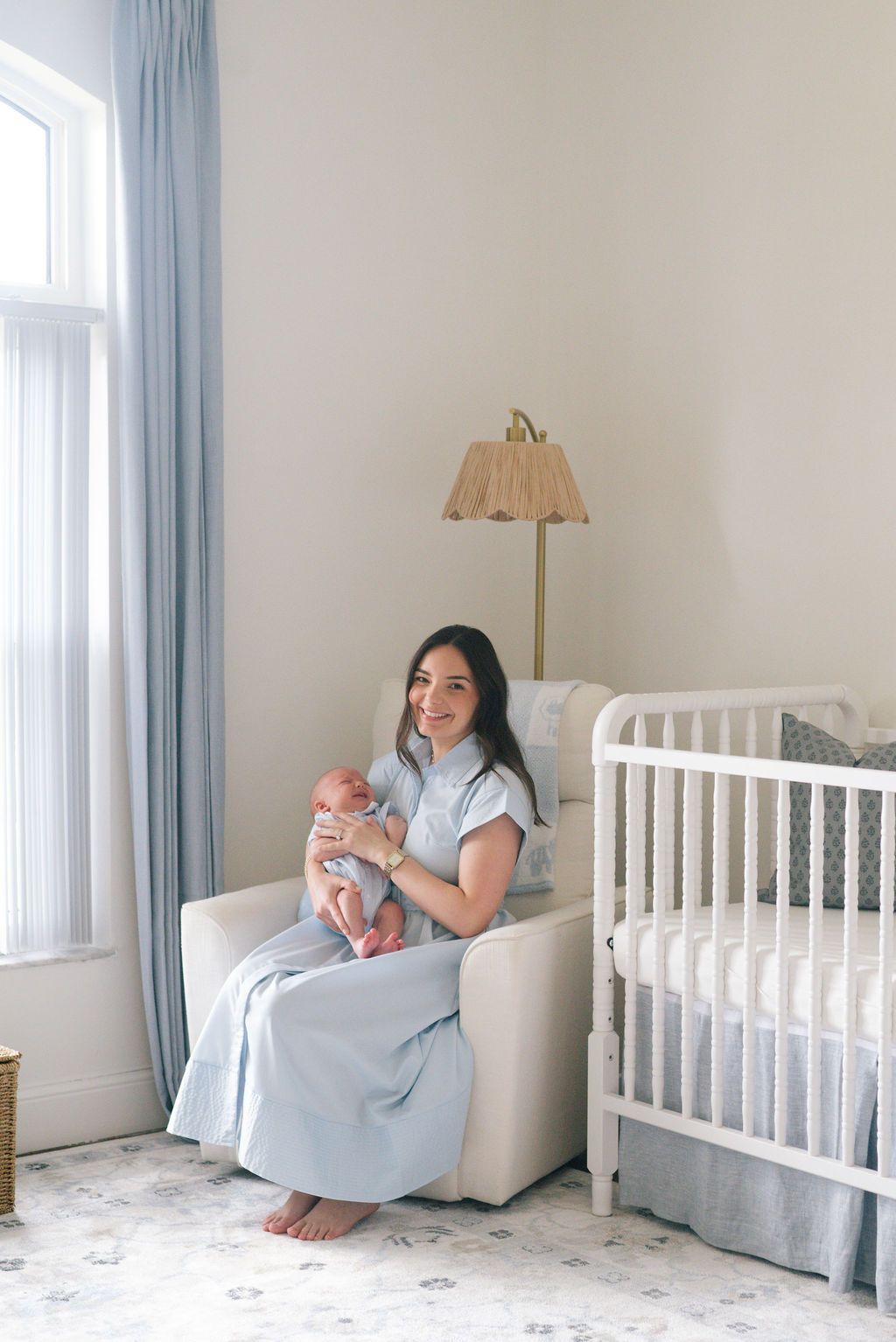 Bright nursery room with light blue curtains, white crib, and comfortable armchair.