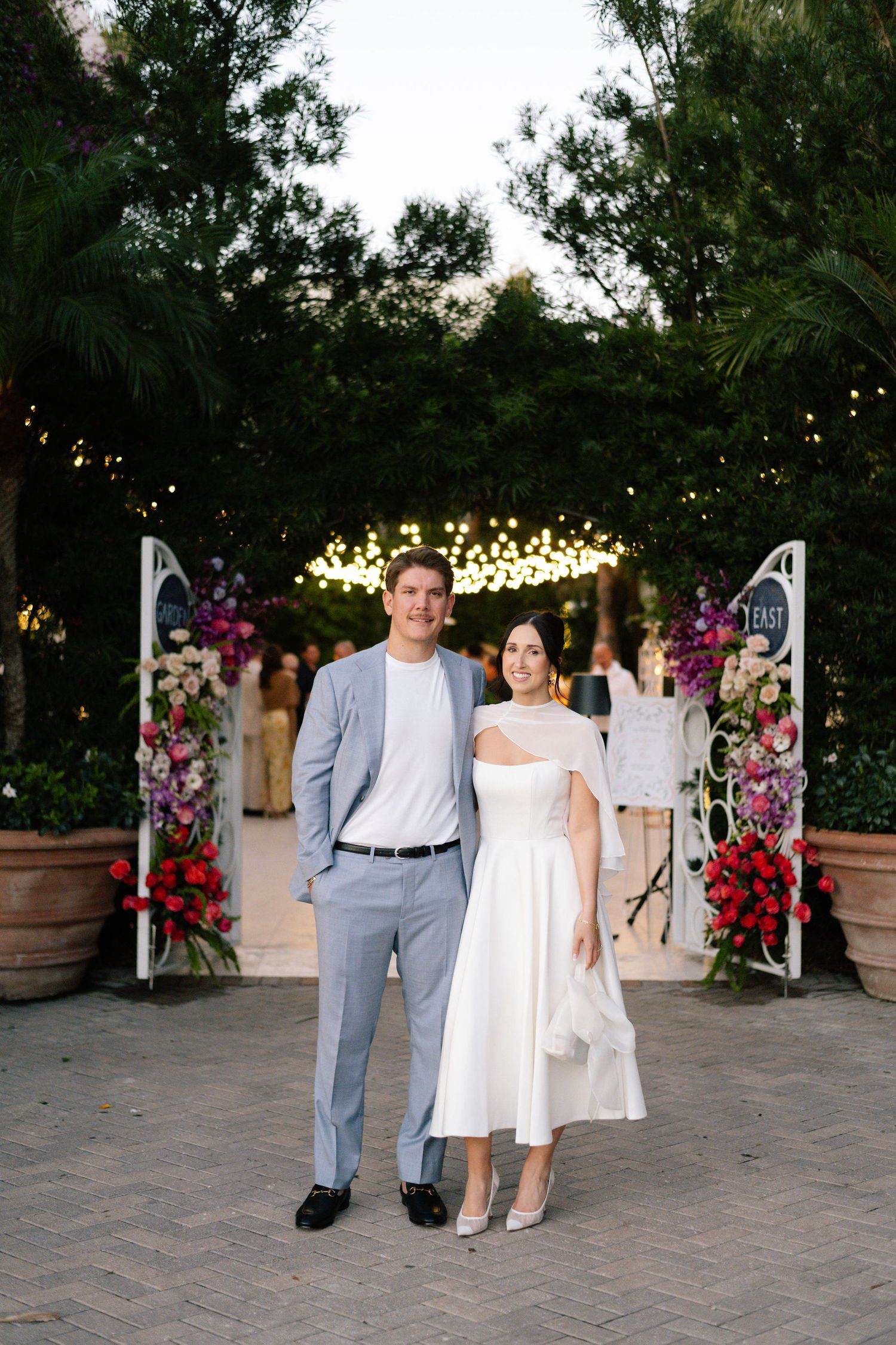 Outdoor wedding venue decorated with string lights and floral arrangements at dusk.