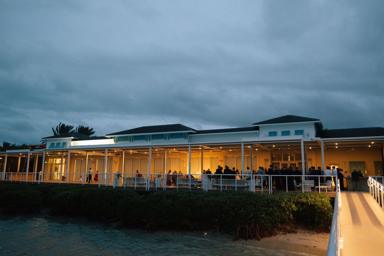 Panoramic view of a modern event venue at dusk with warm interior lighting glowing through large windows.