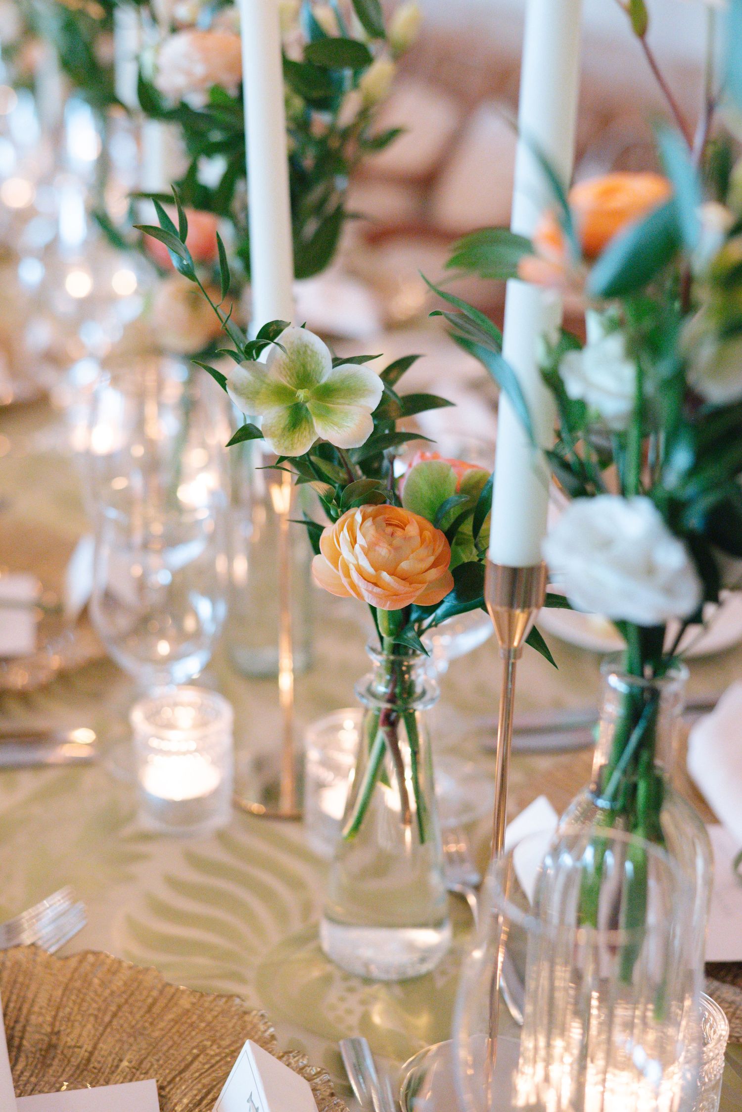 Close-up of wedding centerpieces with peach roses and white lilies in glass vases with tall white candles.