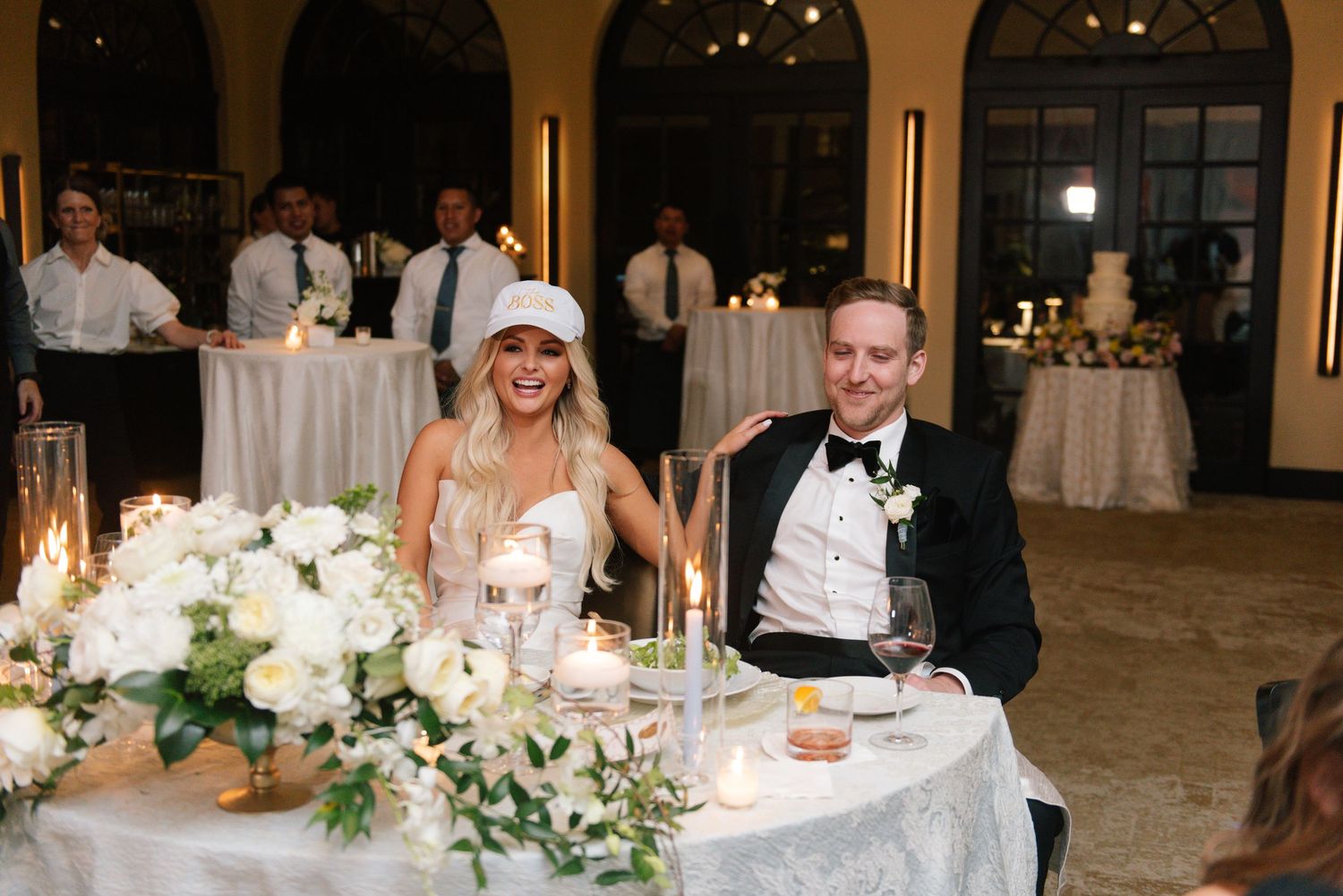 Wedding reception table decorated with white floral arrangements and glowing candles.
