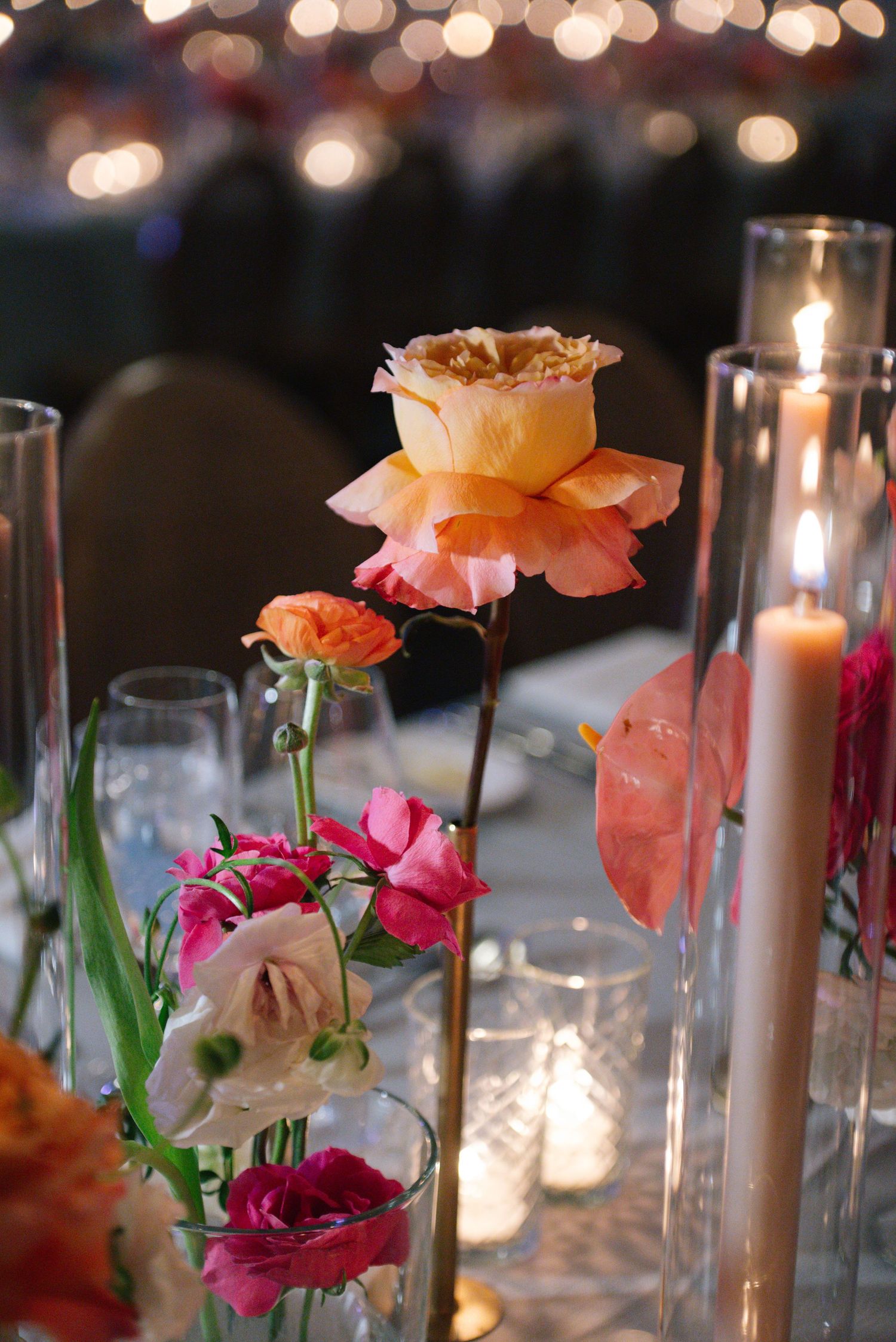 Candlelit table settings with pink and peach roses in glass vases create an elegant dining atmosphere.