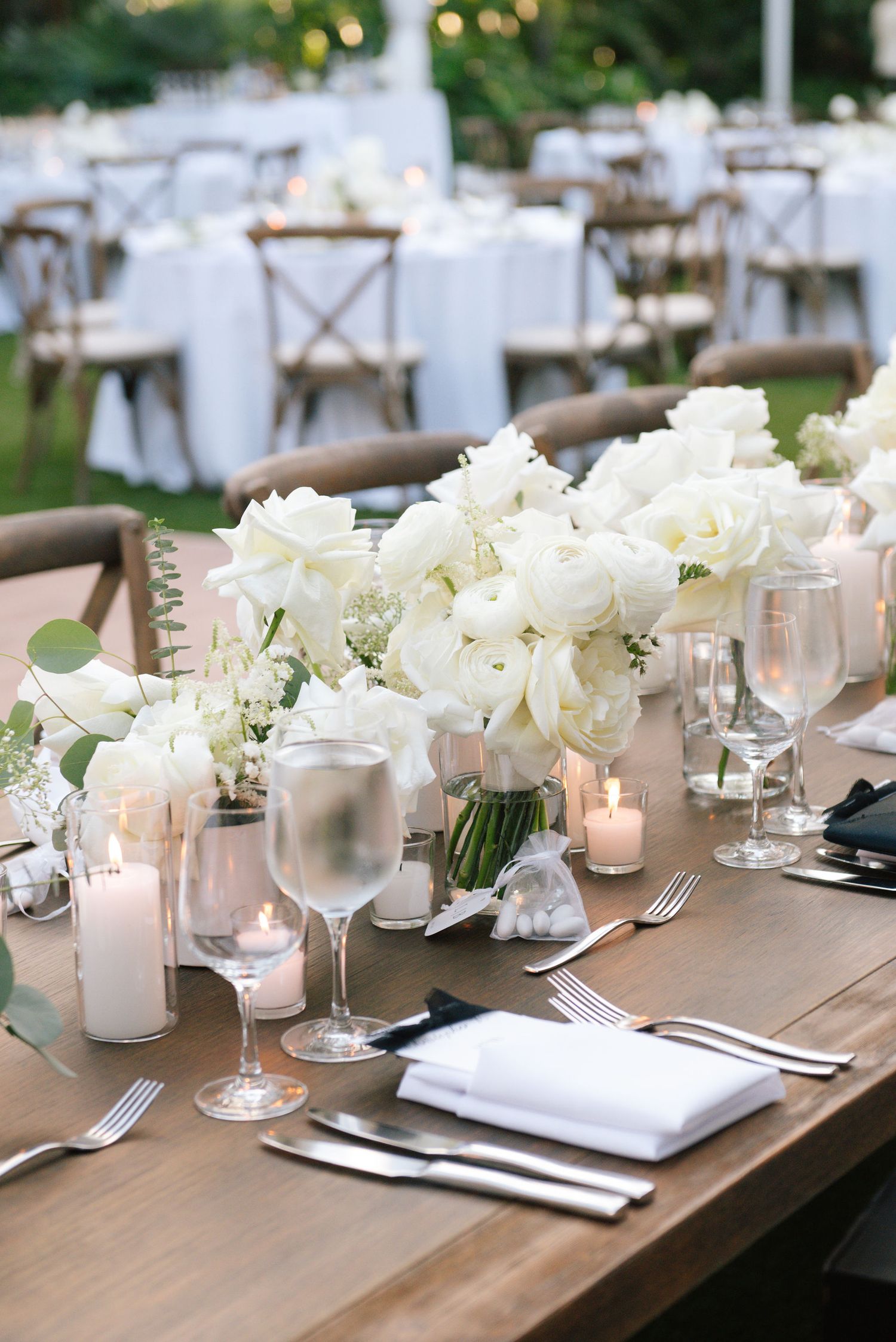 White floral arrangements and glowing candles decorate a rustic wooden table with formal place settings.
