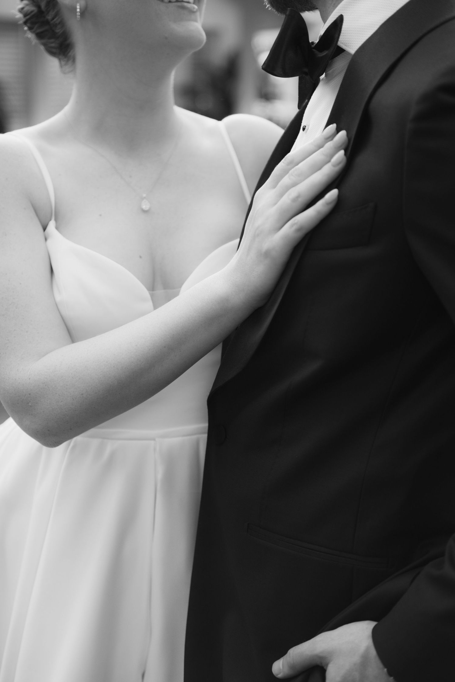 Close-up black and white photo showing details of formal wedding attire with a delicate hand placement.