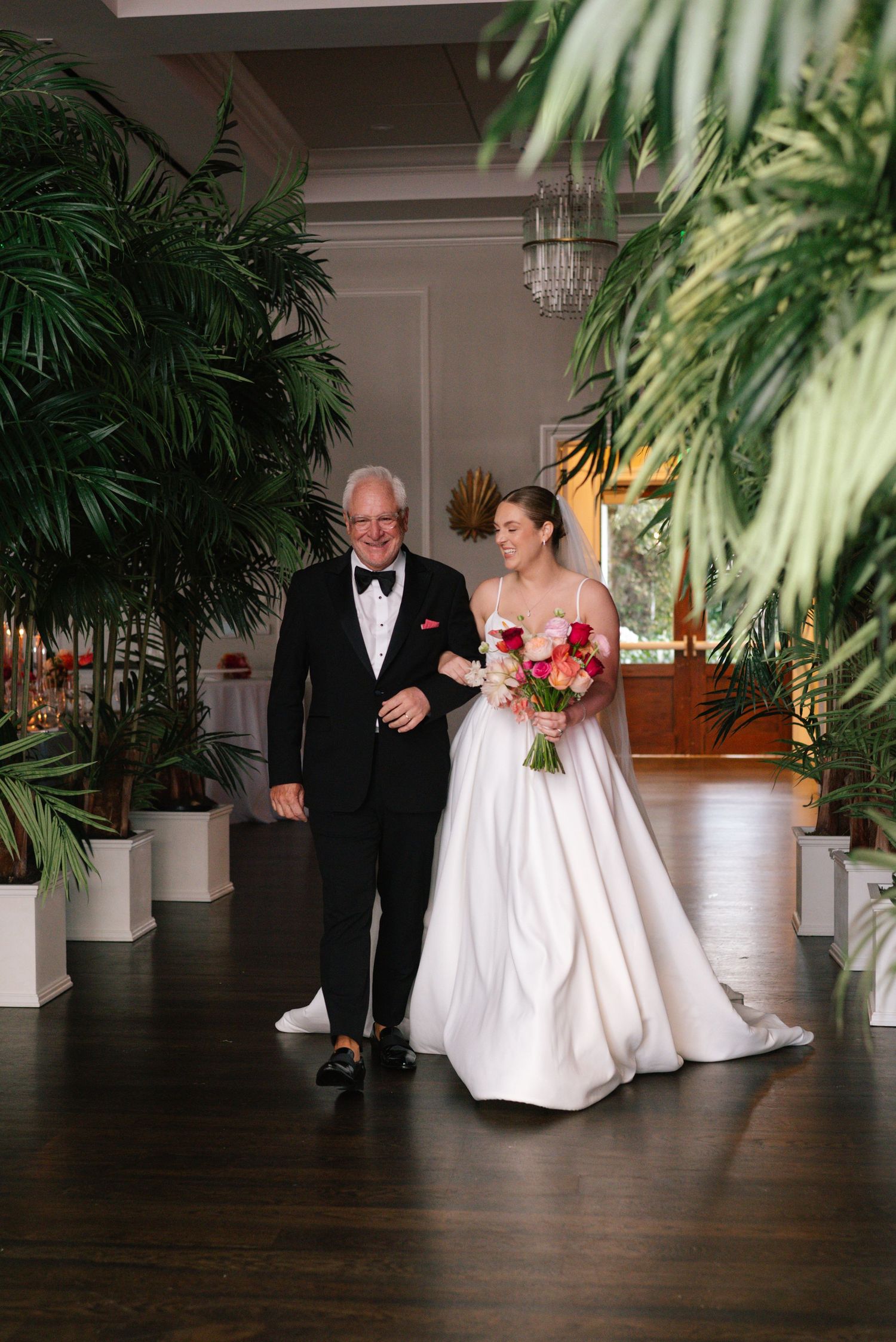 Wedding ceremony processional in elegant indoor venue with tropical plants.