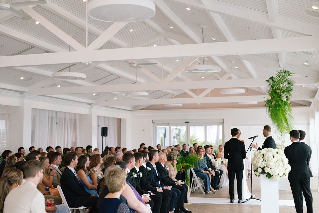 Wedding ceremony panorama showing white architectural details and seated guests.