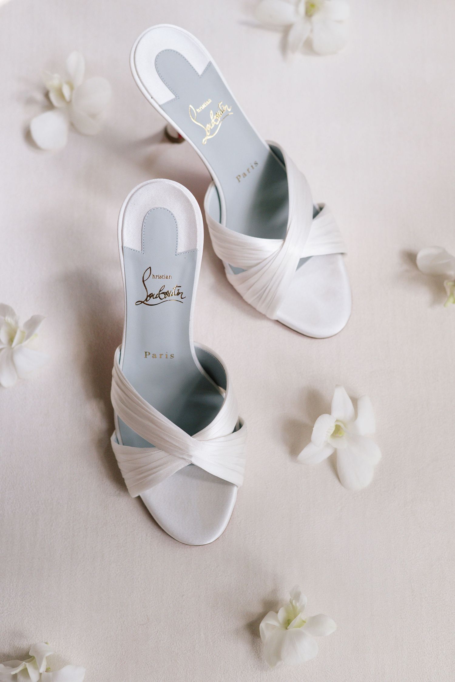 White bridal sandals with crossed straps surrounded by delicate white flower petals.