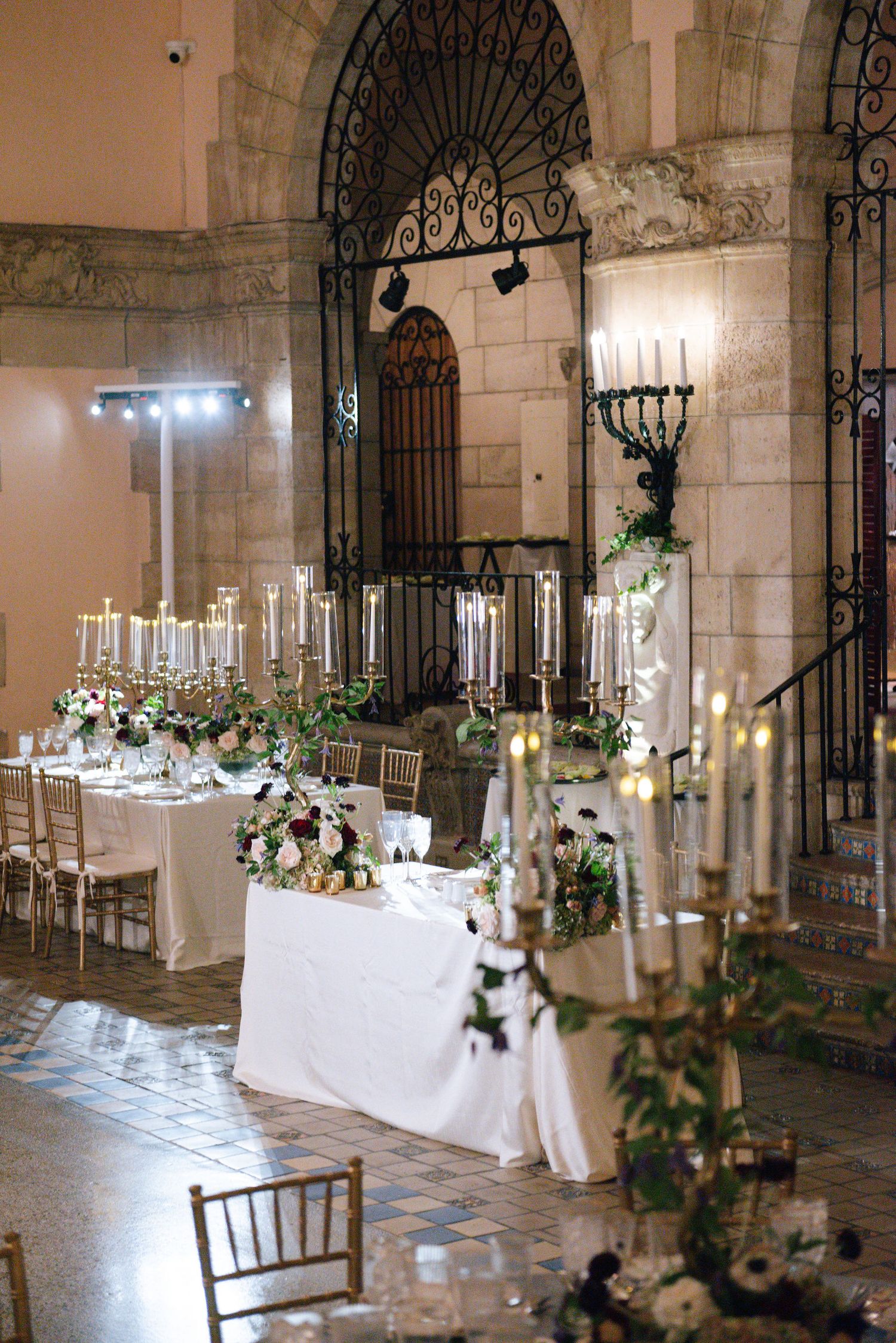 Elegant wedding reception setup with candelabras and white linens under arched stone doorways.