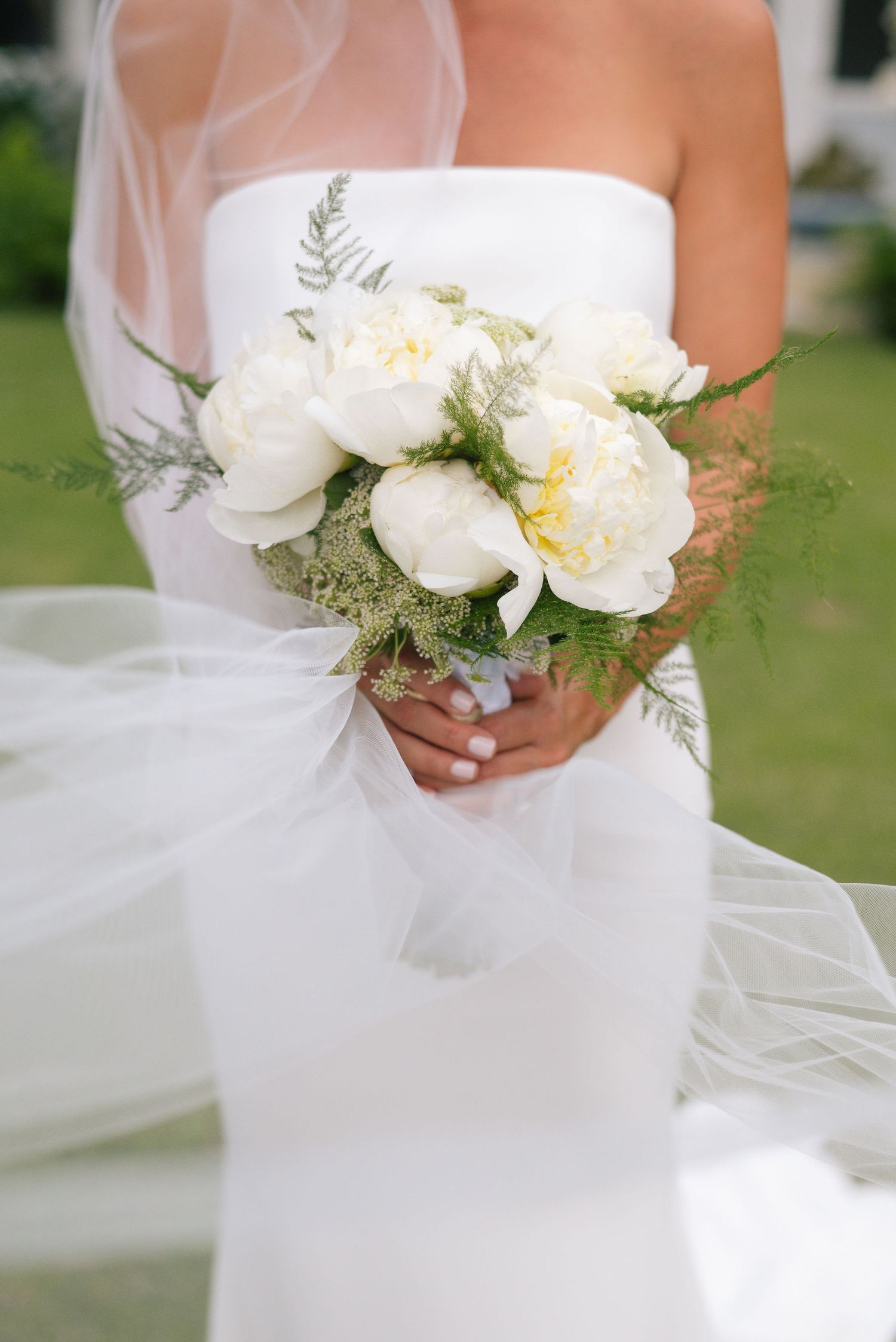 Close-up of white orchid and greenery bridal bouquet against flowing wedding dress fabric.