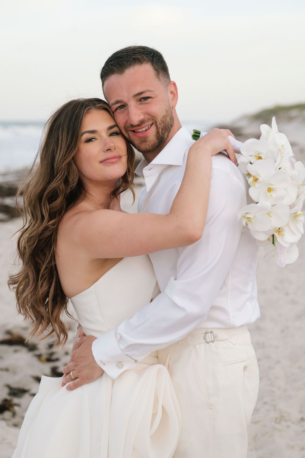 Romantic beach portraits with white orchid bouquet and matching attire.