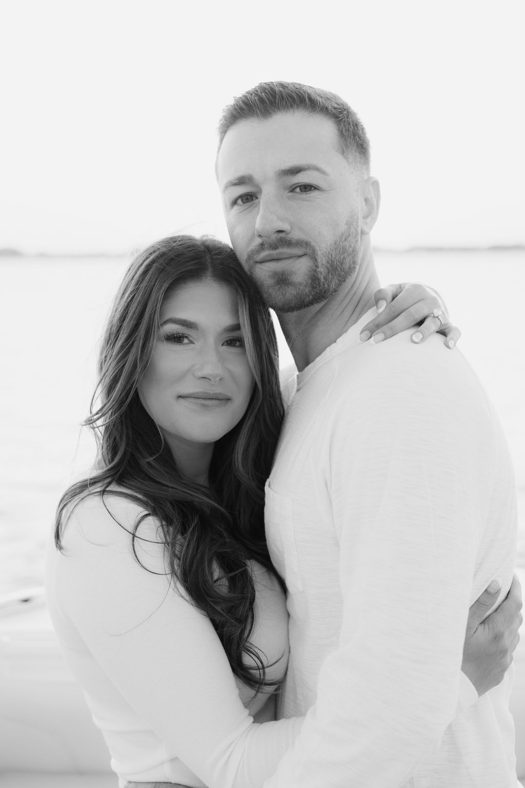 Couple in white embracing on a boat against ocean backdrop.
