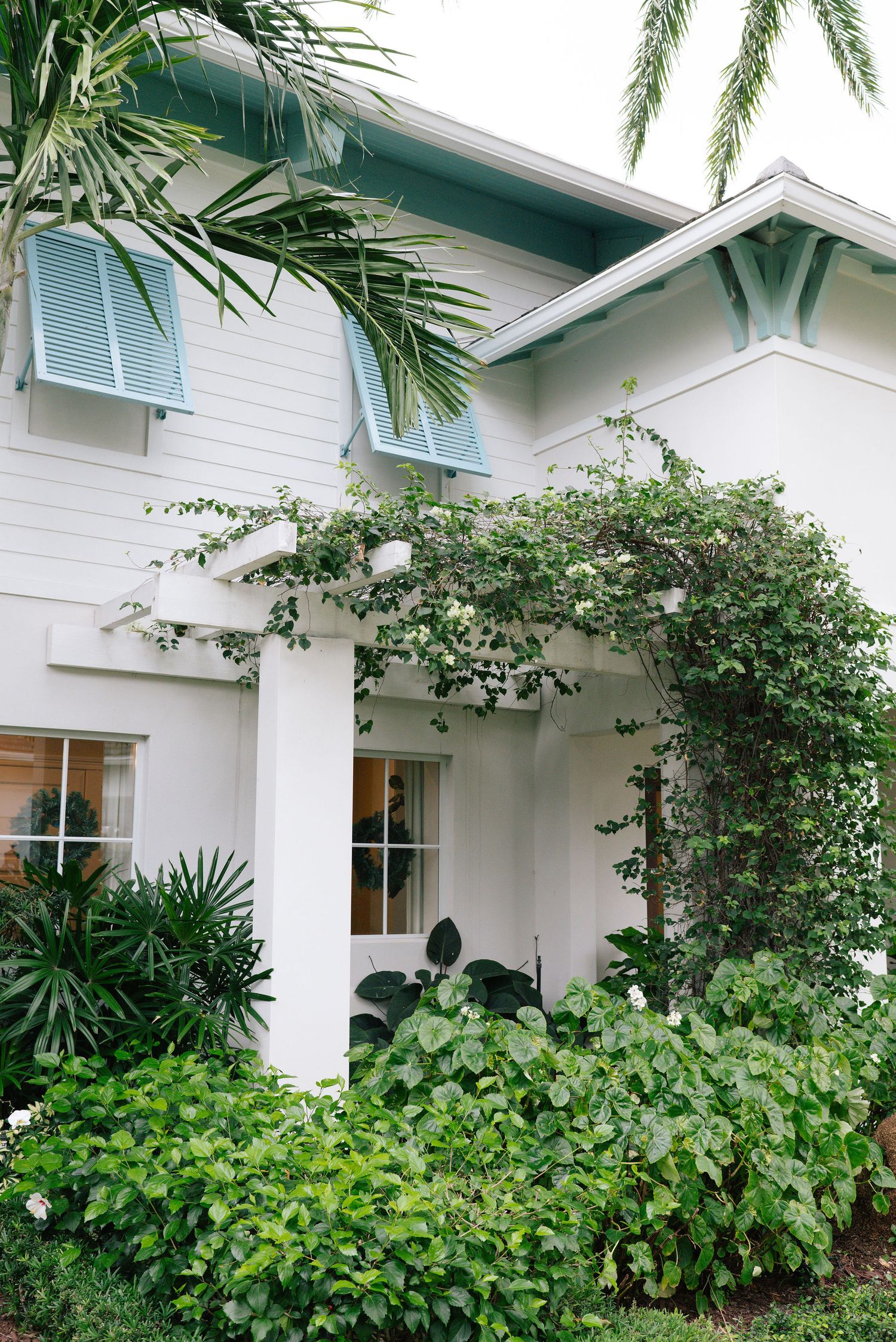 White coastal-style house with climbing roses and tropical landscaping.