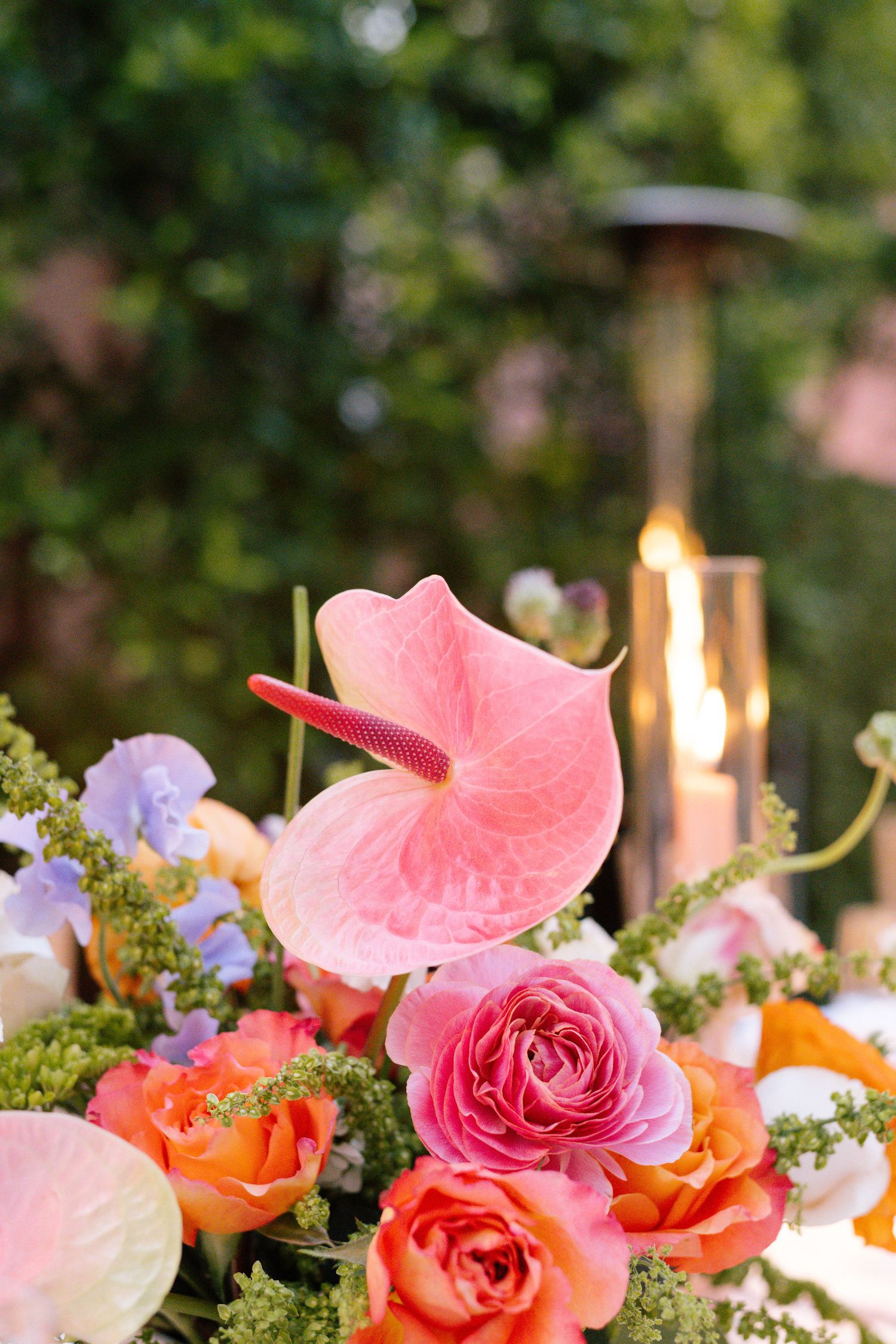 Close-up of coral roses, pink anthurium, and orange flowers in wedding table arrangement.