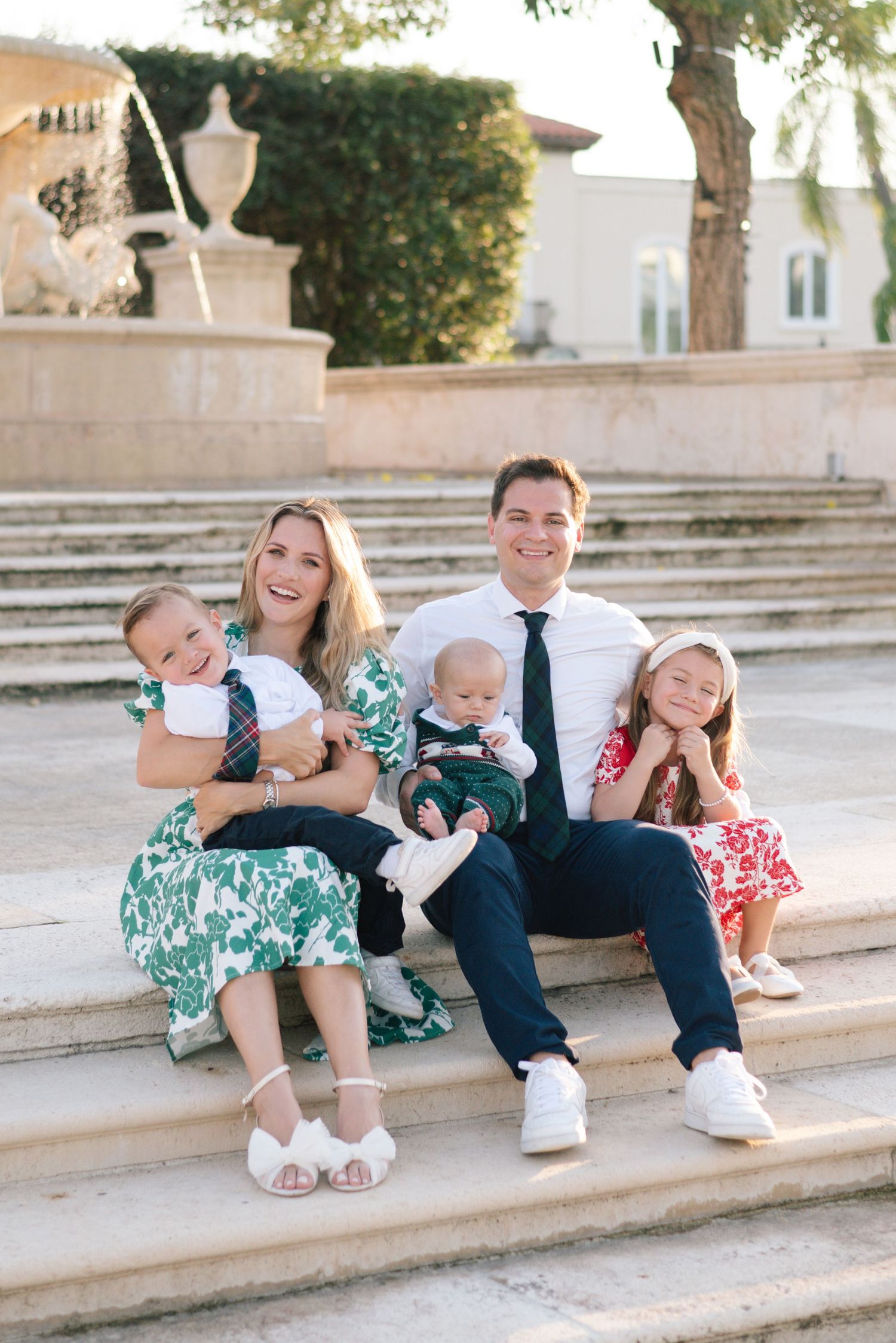 Family with young children sits casually on stone steps for outdoor portrait session.