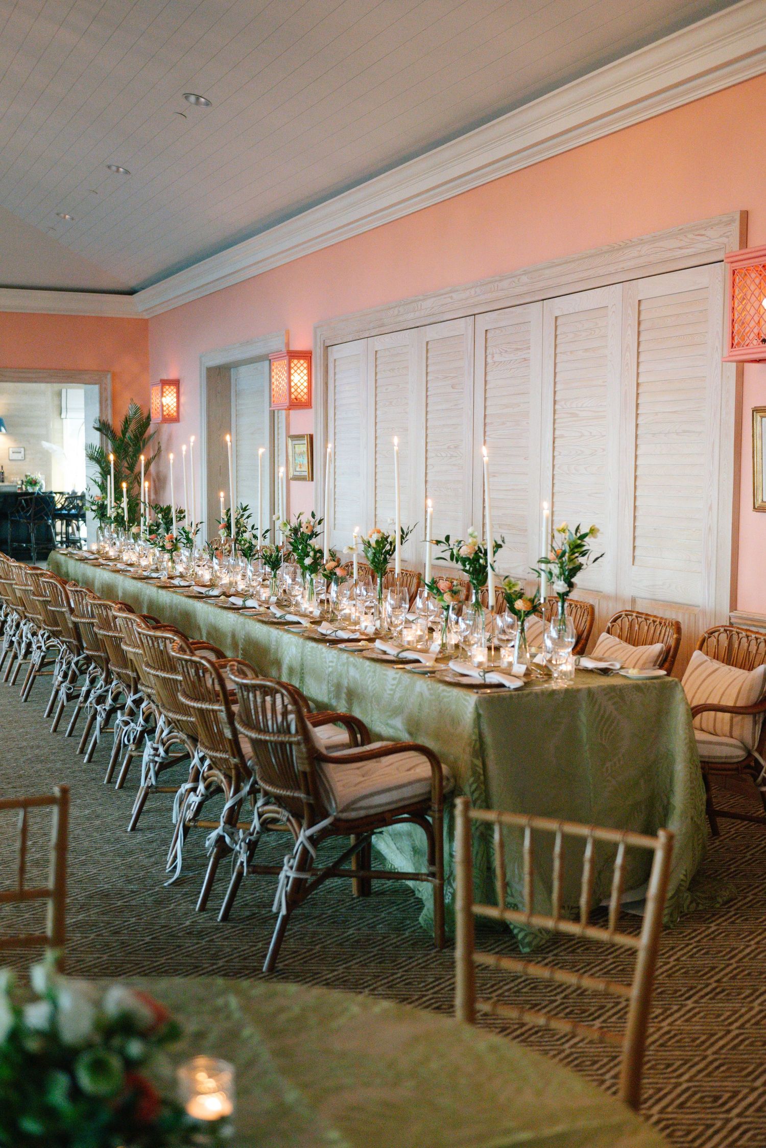 Elegant wedding reception table with green tablecloth, chiavari chairs, and floral centerpieces in a peach-toned room.