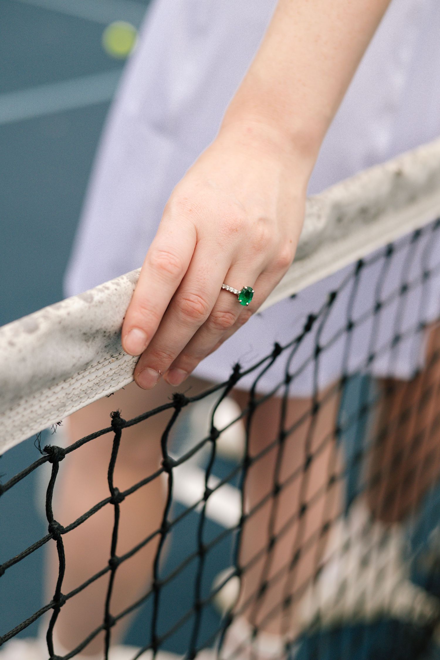 Hand touching black tennis net mesh against blurred court background.
