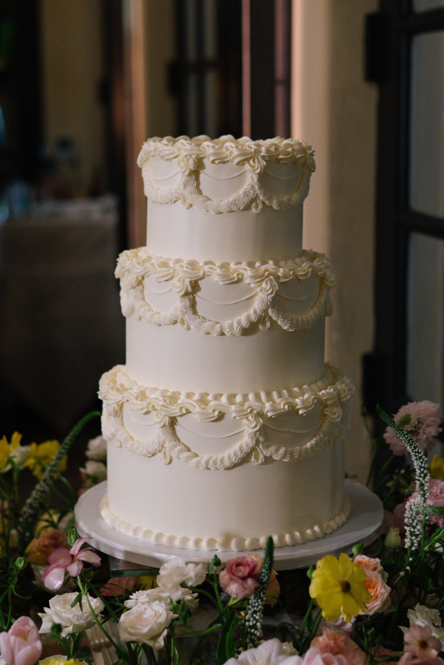 Classic three-tier white wedding cake decorated with piped swags and floral accents.