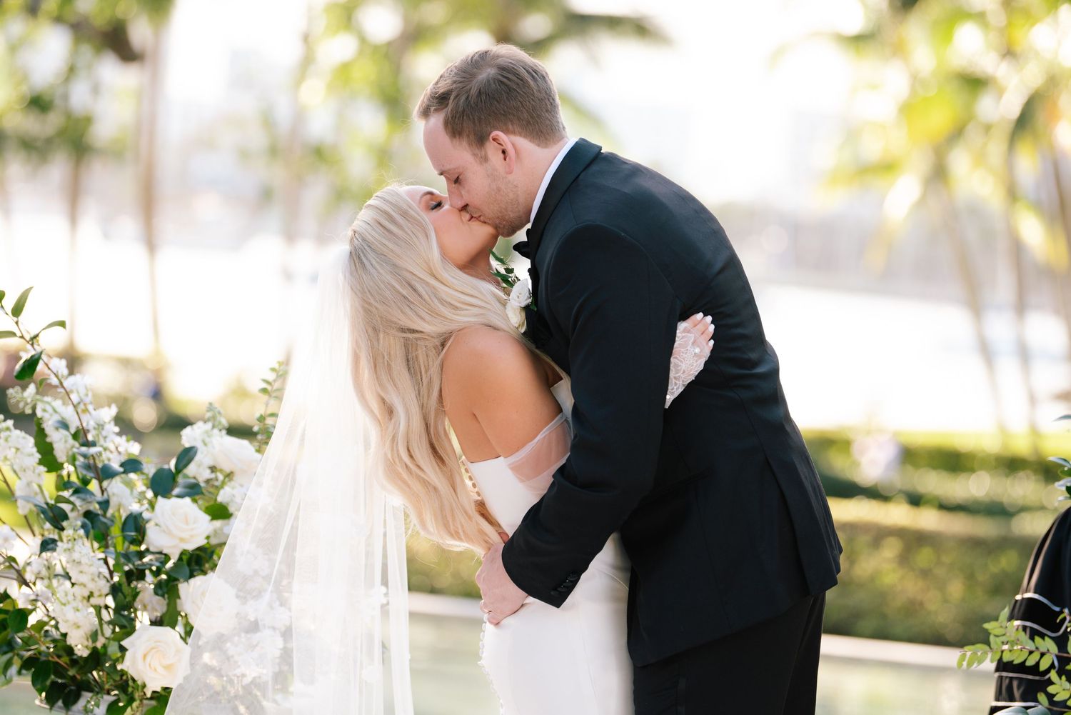 A couple shares a romantic kiss in a lush garden setting during their wedding ceremony.